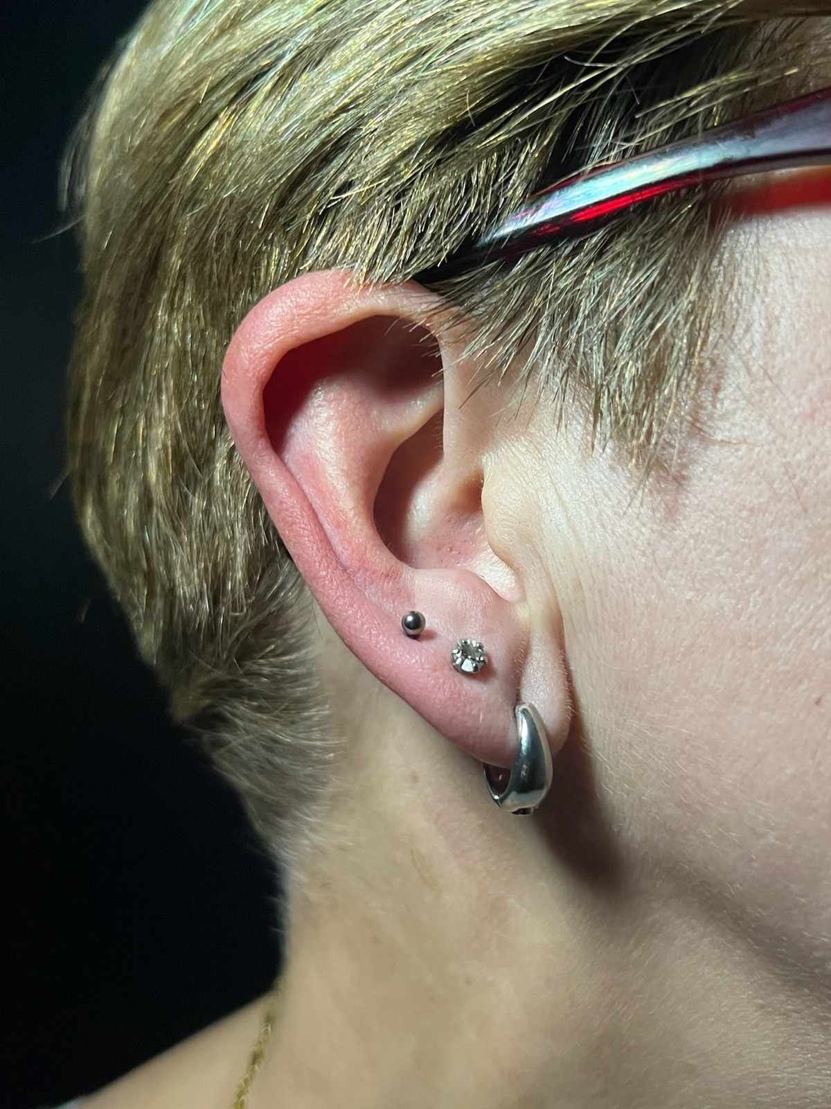 Primer plano de la oreja de una persona con múltiples perforaciones, incluidos tachuelas y un pendiente de aro.