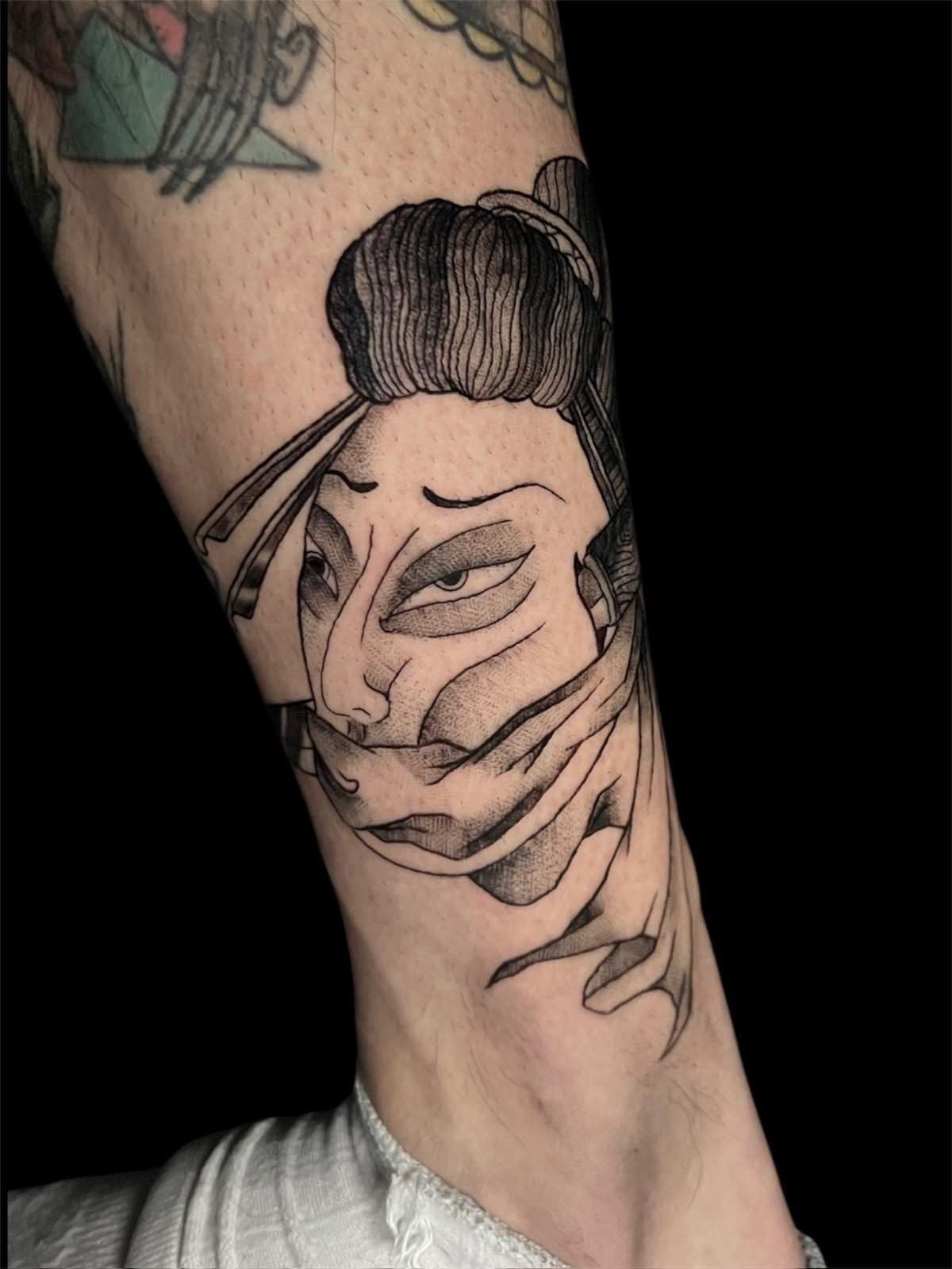 Tatuaje en blanco y negro de la cara de una geisha japonesa en una pierna, mirando hacia abajo.