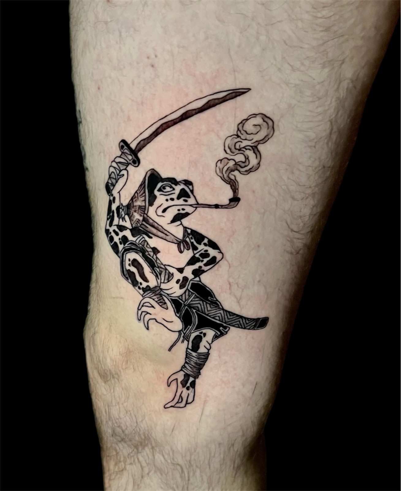 Tatuaje de un samurái rana con una katana y fumando una pipa en la pierna de una persona.