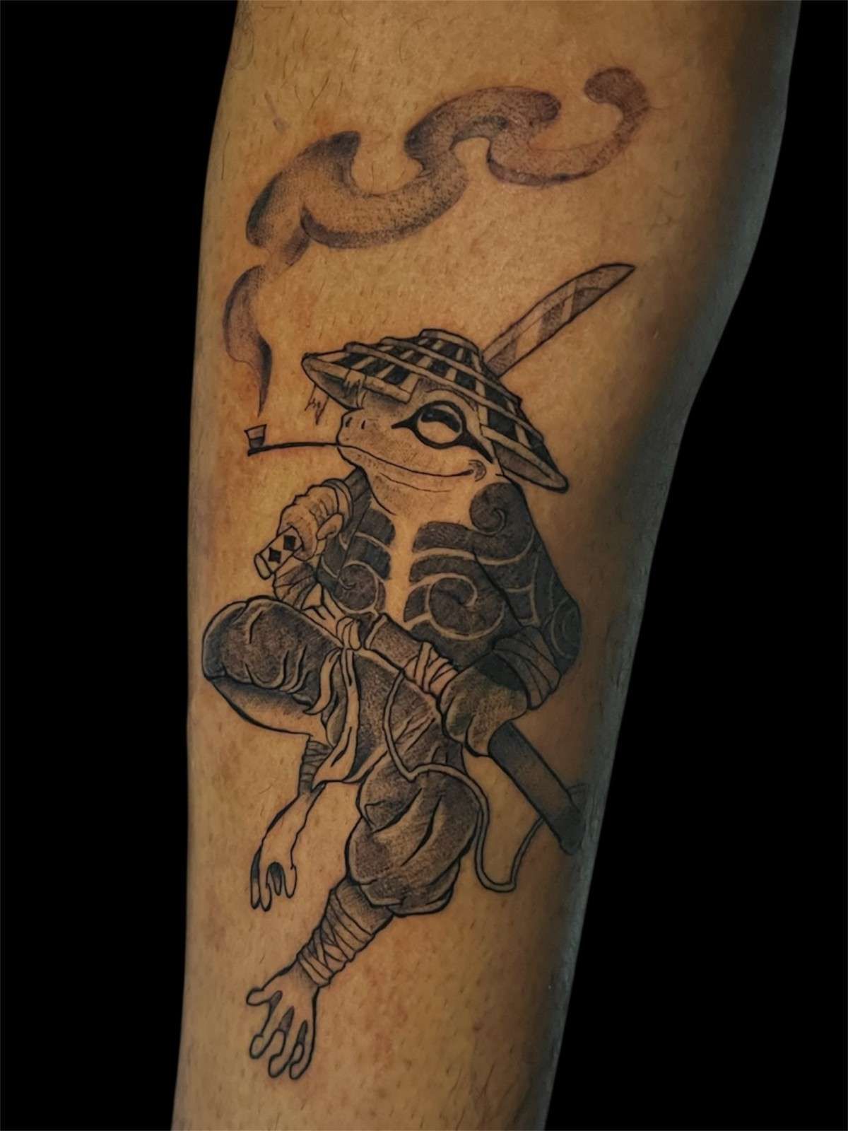 Tatuaje de una rana ninja con sombrero, sosteniendo un cigarrillo, humo encima.