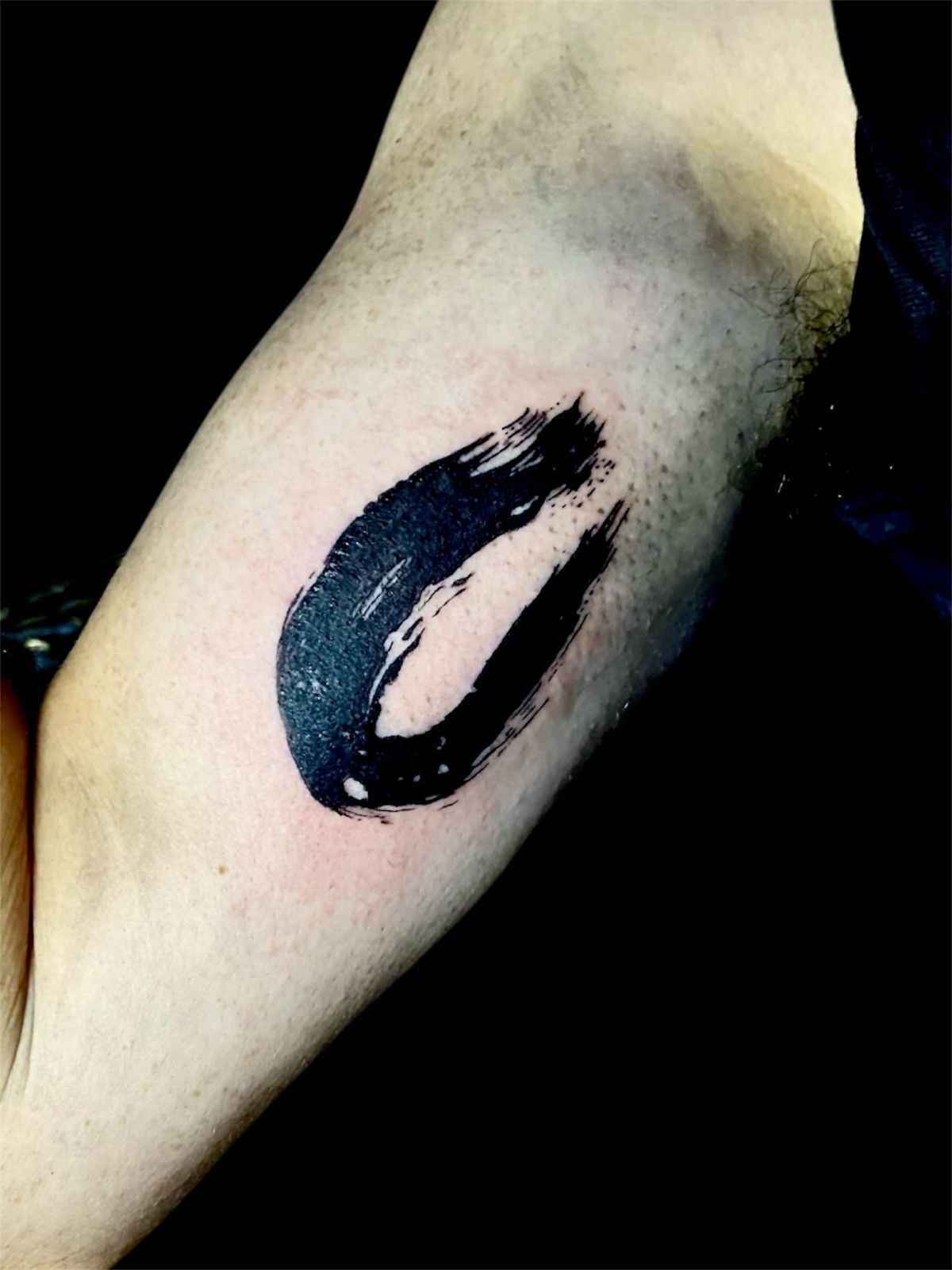 Tatuaje de círculo Enso en tinta negra en el brazo de una persona.