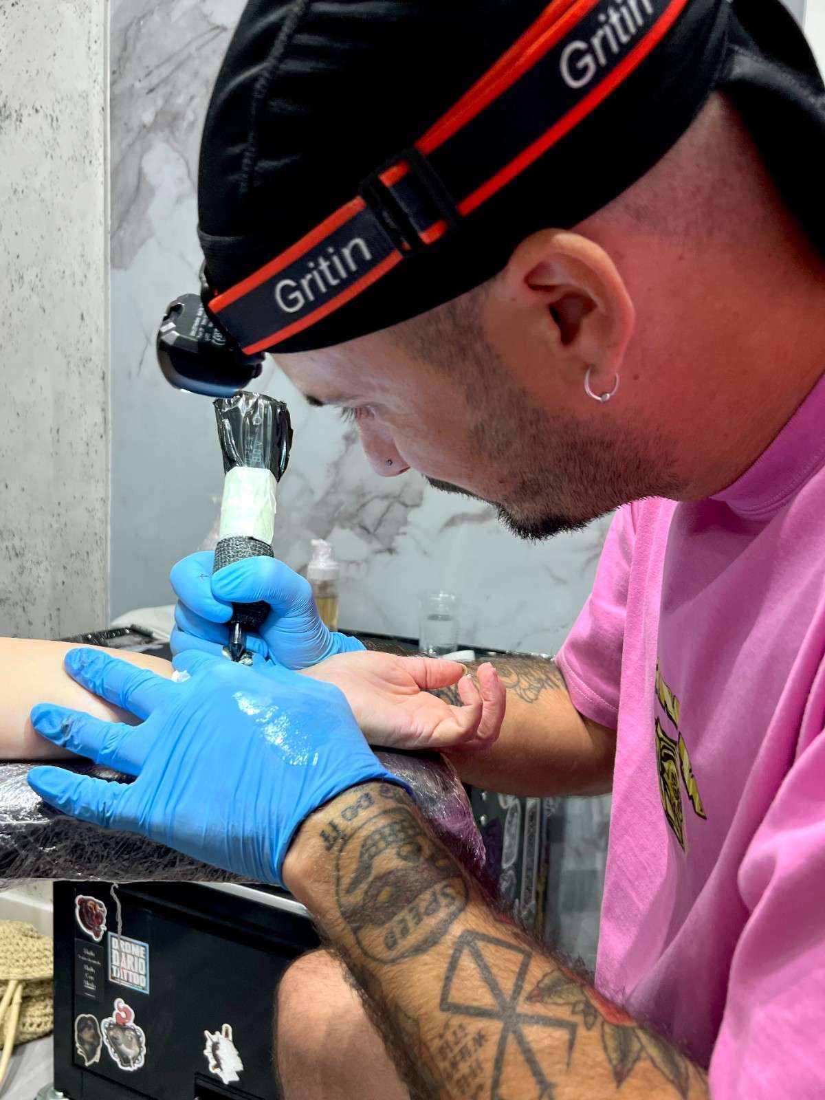 Hombre que lleva un gorro negro y una sudadera con capucha, de pie frente a una pared de mármol.