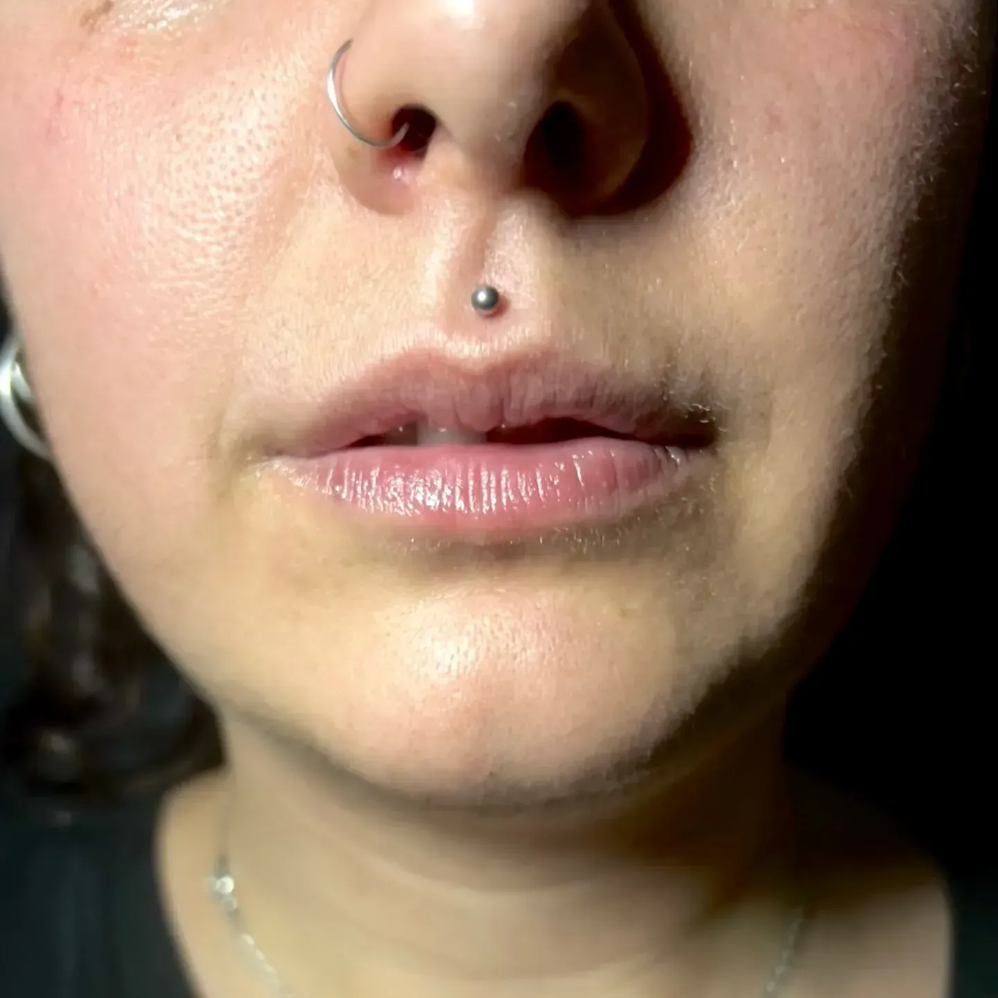 Primer plano del rostro de una persona con un piercing en el labio superior y un anillo en la nariz.