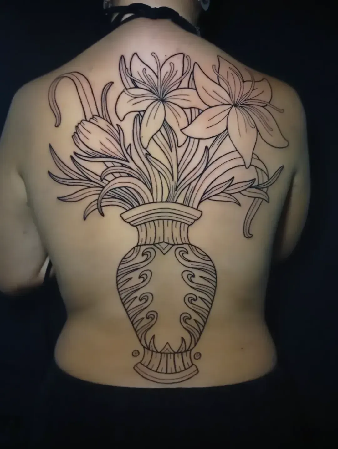 Tatuaje de línea negra de un arreglo floral en un jarrón en la espalda de una persona.