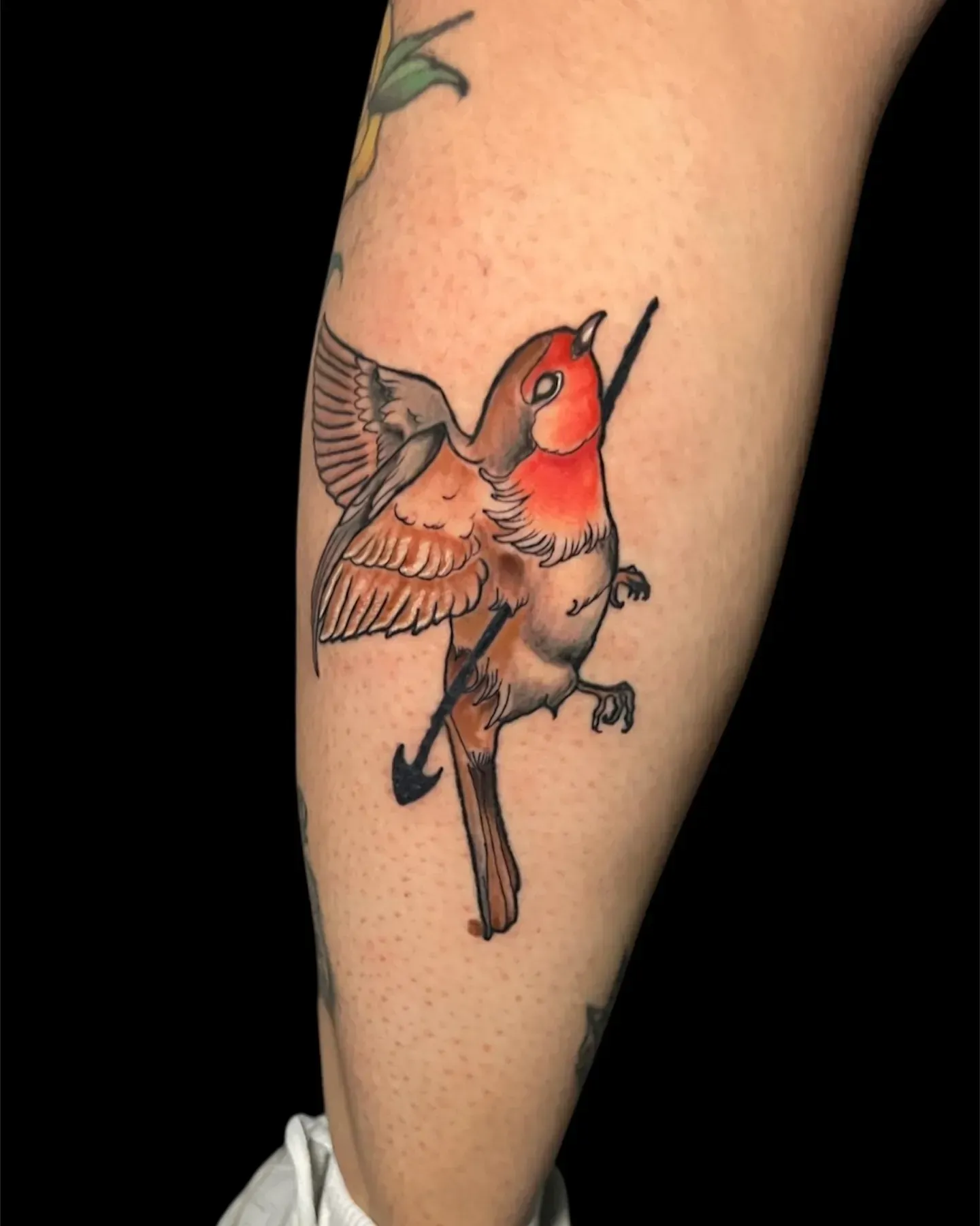 Tatuaje de un petirrojo atravesado por una flecha. El ave tiene el pecho rojo, alas marrones