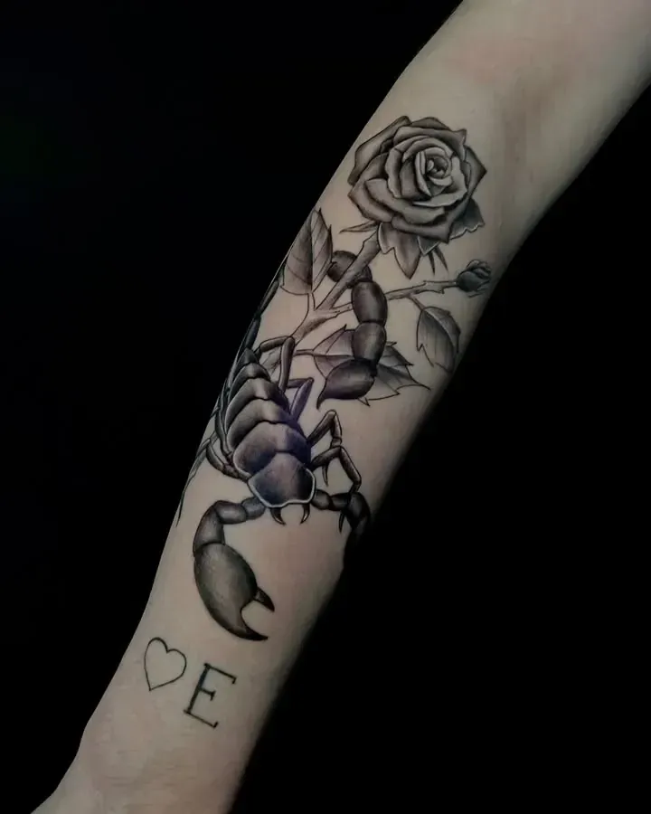Tatuaje de un escorpión negro y gris y una rosa en un brazo, con un corazón y un tatuaje de la letra 