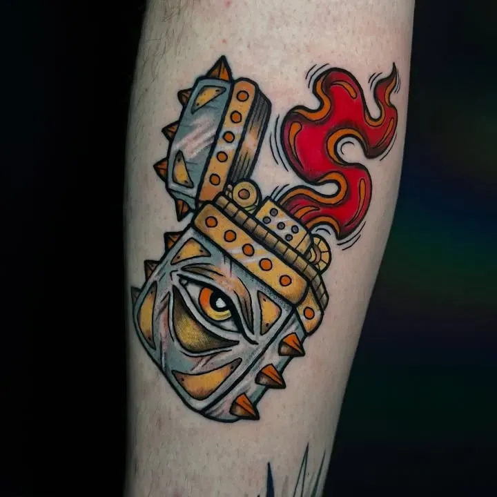 Tatuaje de un encendedor estilizado con un ojo, llamas y púas, en el brazo de una persona.