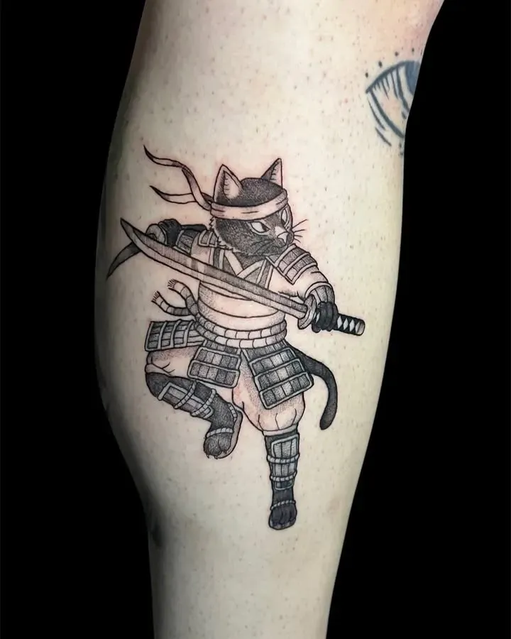 Gato negro con armadura samurái sosteniendo una espada. Tatuaje en la pierna.