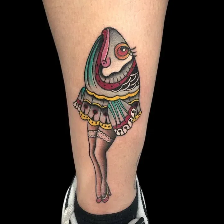 Tatuaje de un pez estilizado con pierna humana, vestido con falda y medias.