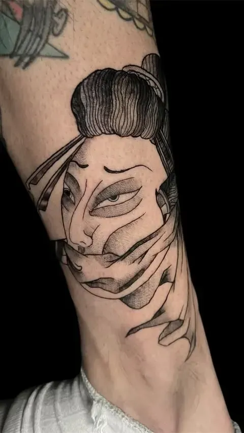 Tatuaje de una geisha estilizada, con el rostro distorsionado como si se desgarrara, en un brazo, líneas blancas y negras.