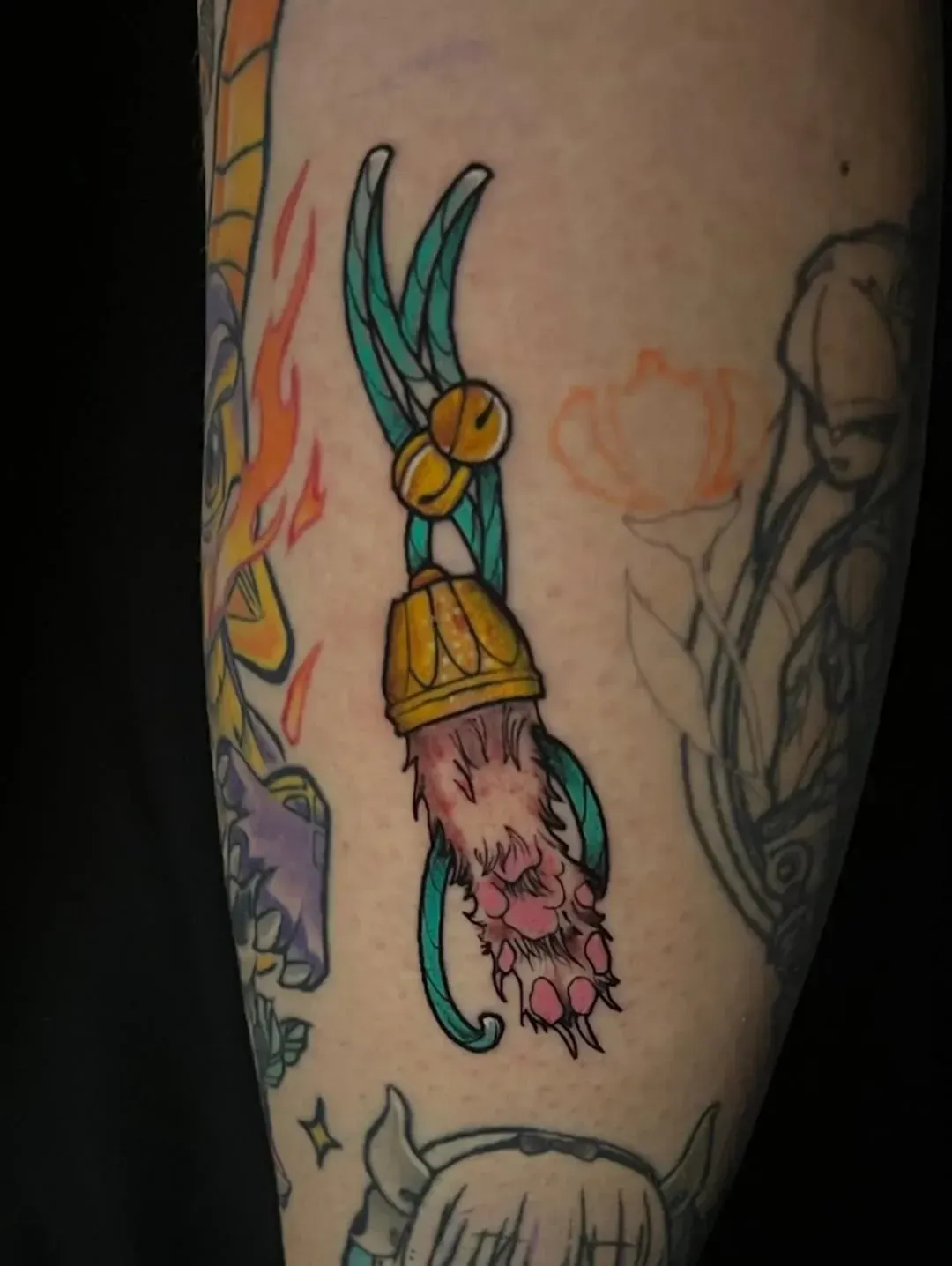 Tatuaje de una pata de conejo con una corona, campanas y remolinos azules en el brazo de una persona