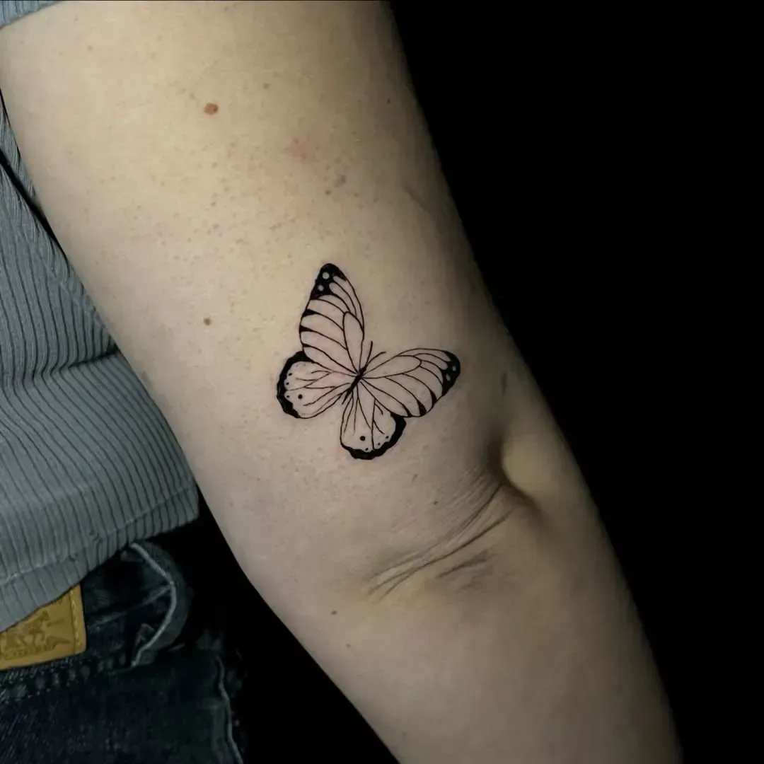 Tatuaje de mariposa en la parte interna del brazo. Alas detalladas en blanco y negro.