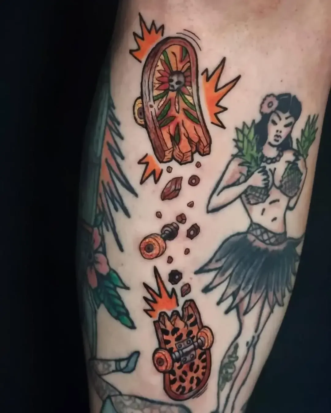 Tatuaje de una patineta rota explotando sobre una bailarina de hula. Tinta naranja, marrón y negra.
