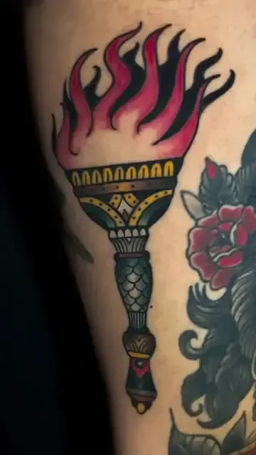 Tatuaje de una antorcha encendida en estilo tradicional, con llamas rojas y negras.