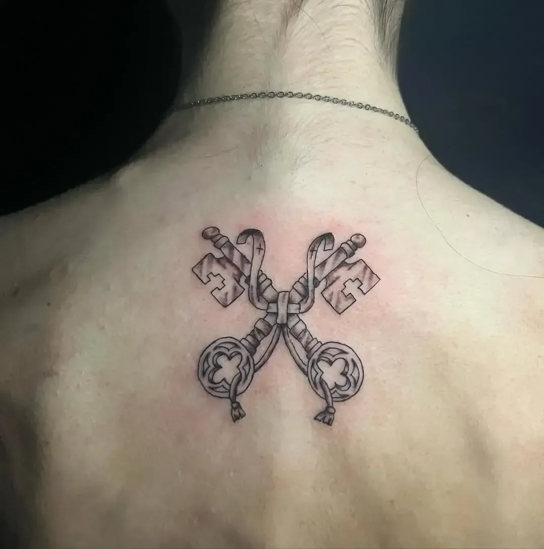 Tatuaje de llaves cruzadas en la espalda. Dos llaves ornamentadas entrelazadas con una cadena.
