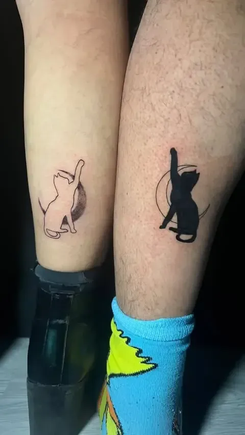 Dos tatuajes de gatos en las piernas: uno de contorno, otro negro sólido, ambos extendiéndose hacia un círculo.