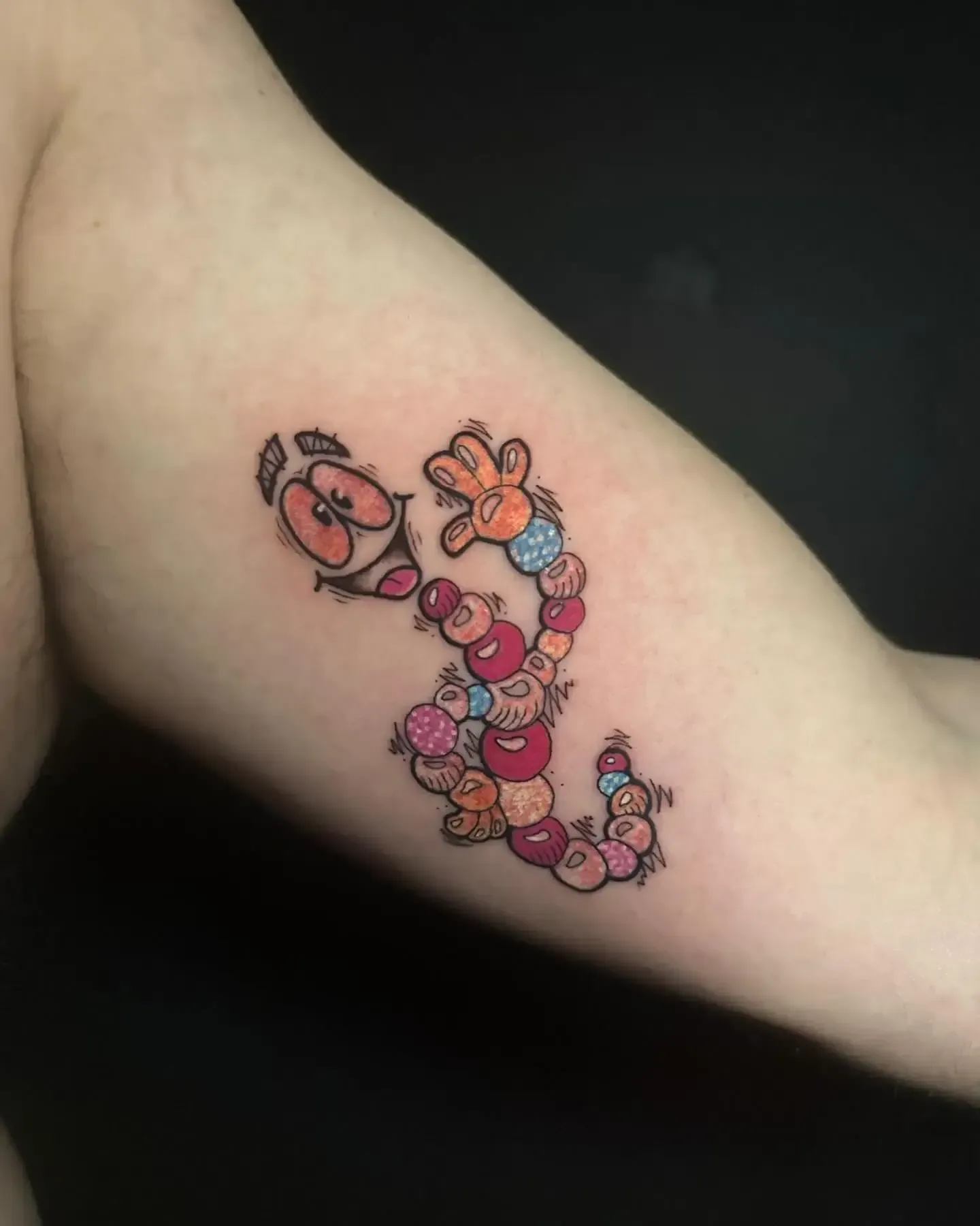 Tatuaje de un gusano de manzana de dibujos animados. Colores brillantes, gusano hecho de frutas, en el brazo.