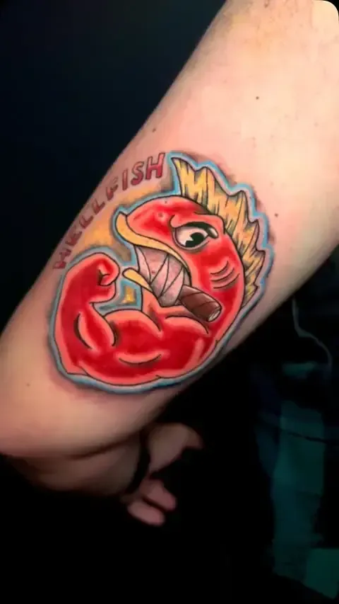 Tatuaje de dibujos animados de un pez rojo flexionando un bíceps, sosteniendo un cigarro, con el texto 