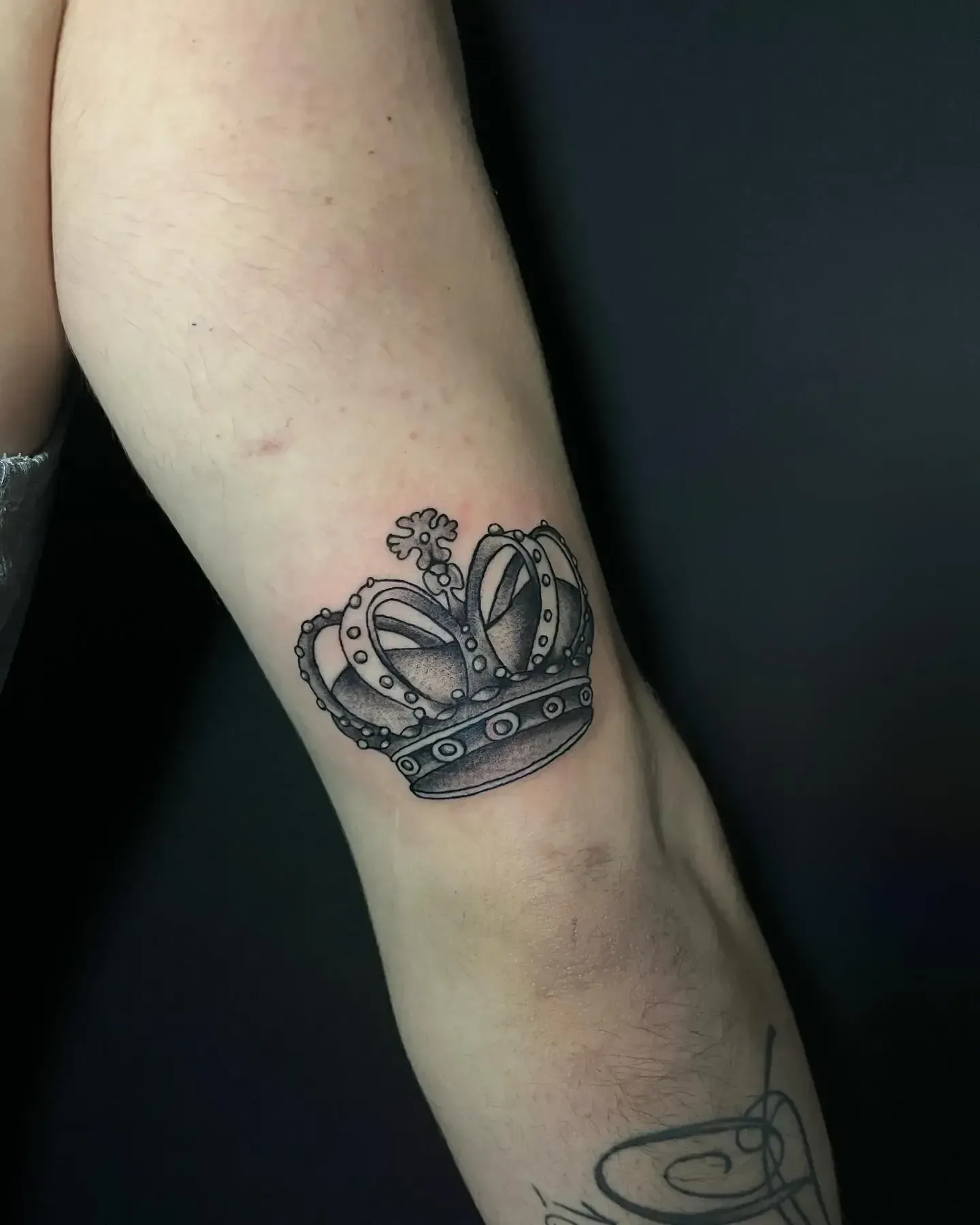 Tatuaje en blanco y negro de una corona en el codo de una persona.