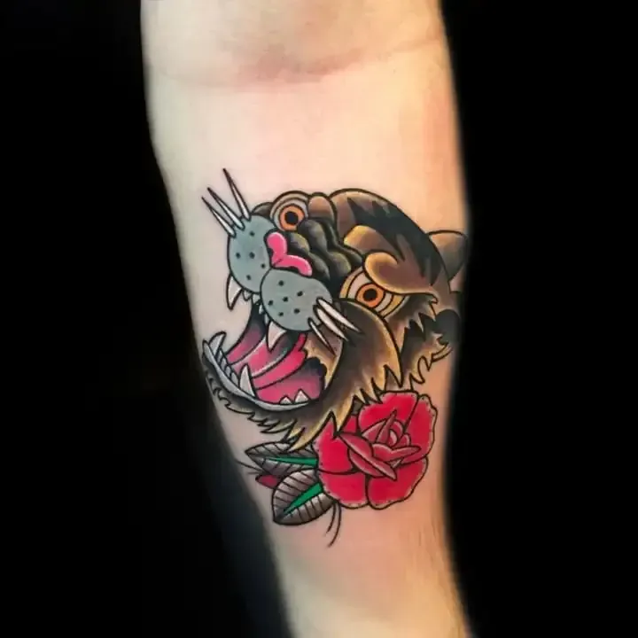 Tatuaje de una cabeza de pantera con la boca abierta, rosa roja, marrón y negra, en un brazo.