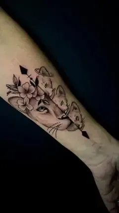 Tatuaje de leona con cachorros y elementos florales. Blanco y negro en el brazo.