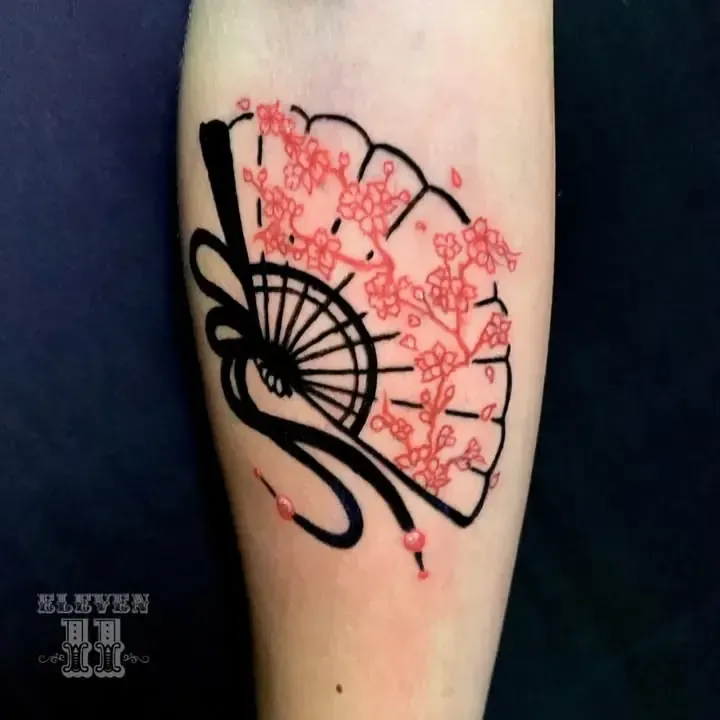 Tatuaje de abanico delineado en negro con ramas de flor de cerezo roja en un brazo de piel clara.