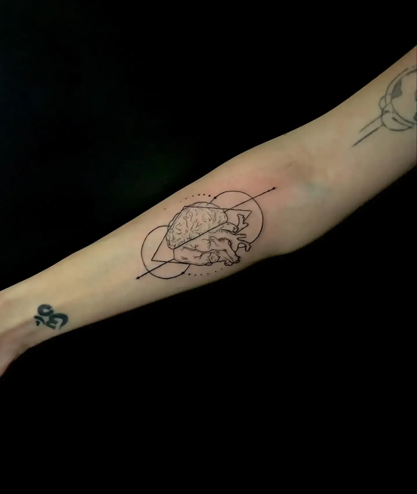 Tatuaje en el brazo: corazón anatómico con líneas geométricas. También hay un pequeño tatuaje de símbolo.