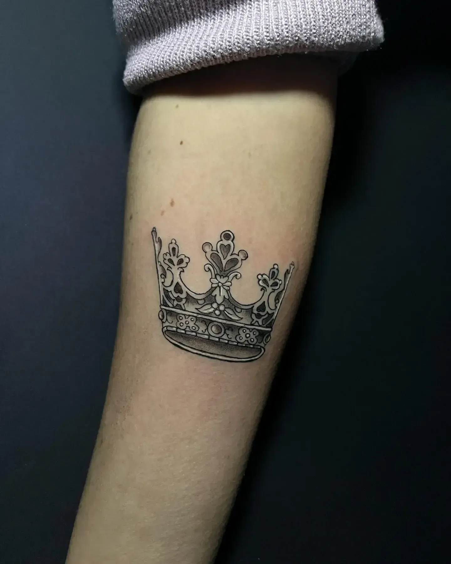 Tatuaje de corona en blanco y negro en el antebrazo de una persona.