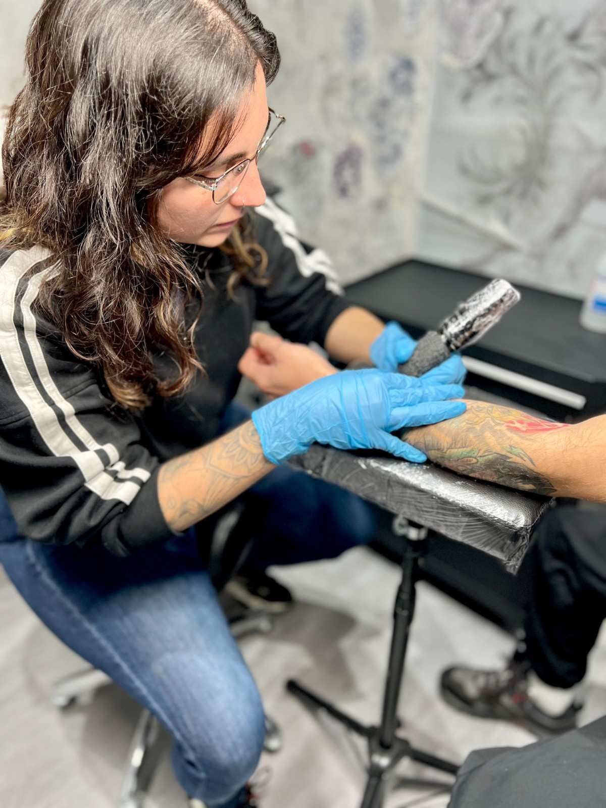 Mujer con gafas, con una chaqueta con estampado de leopardo atada a la cintura, de pie frente a una pared de mármol.