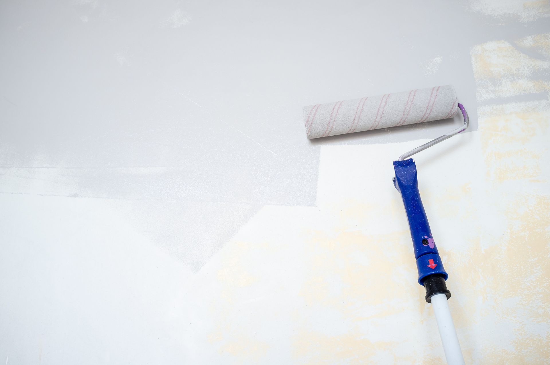 Rodillo de pintura aplicando pintura blanca a una pared.