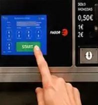 Dedo pulsando el botón verde «START» en la pantalla táctil de una cafetera