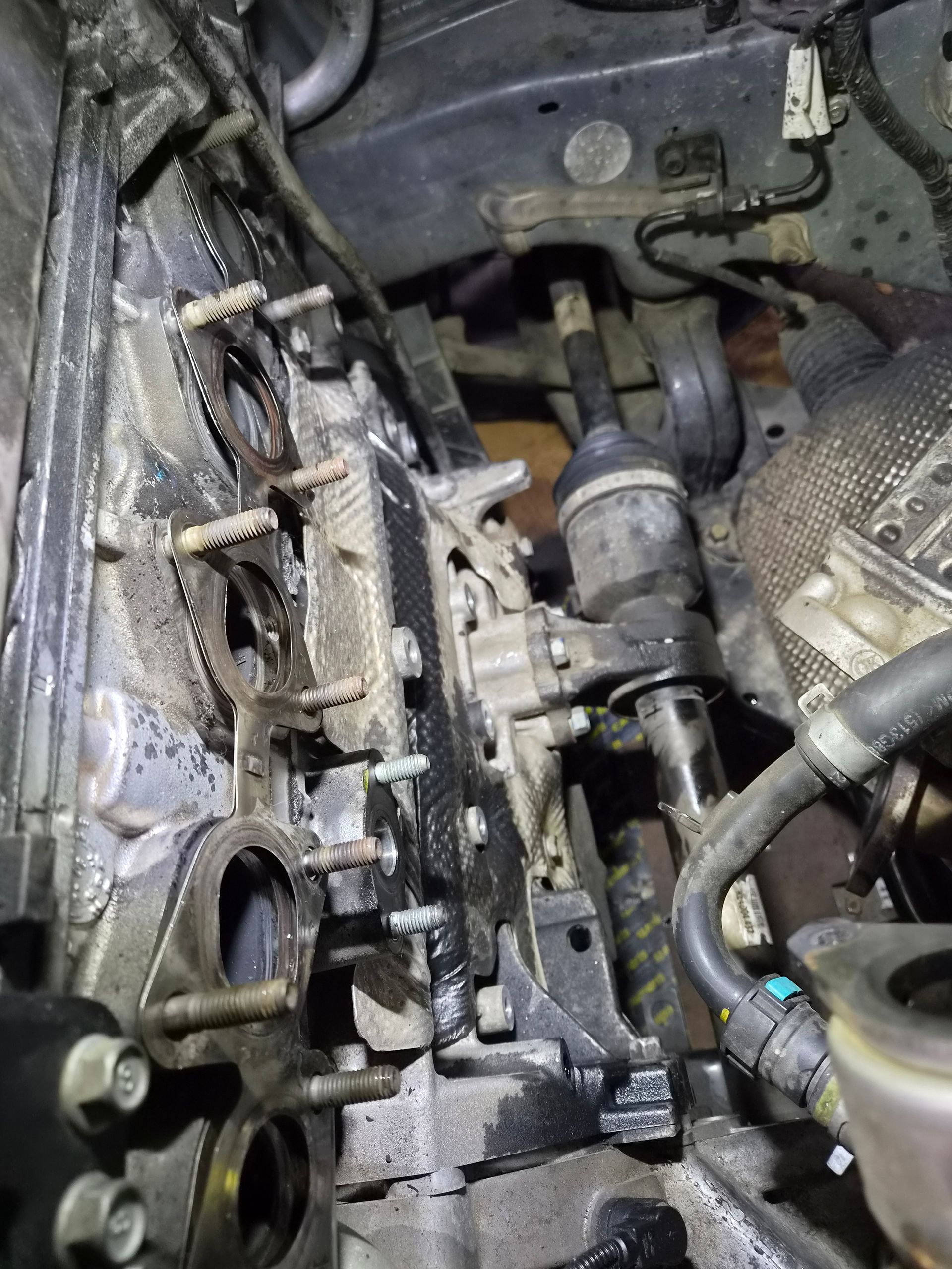 Gros plan sur le compartiment moteur d’une voiture, avec des durites, des câbles et des composants métalliques apparents pendant une réparation.
