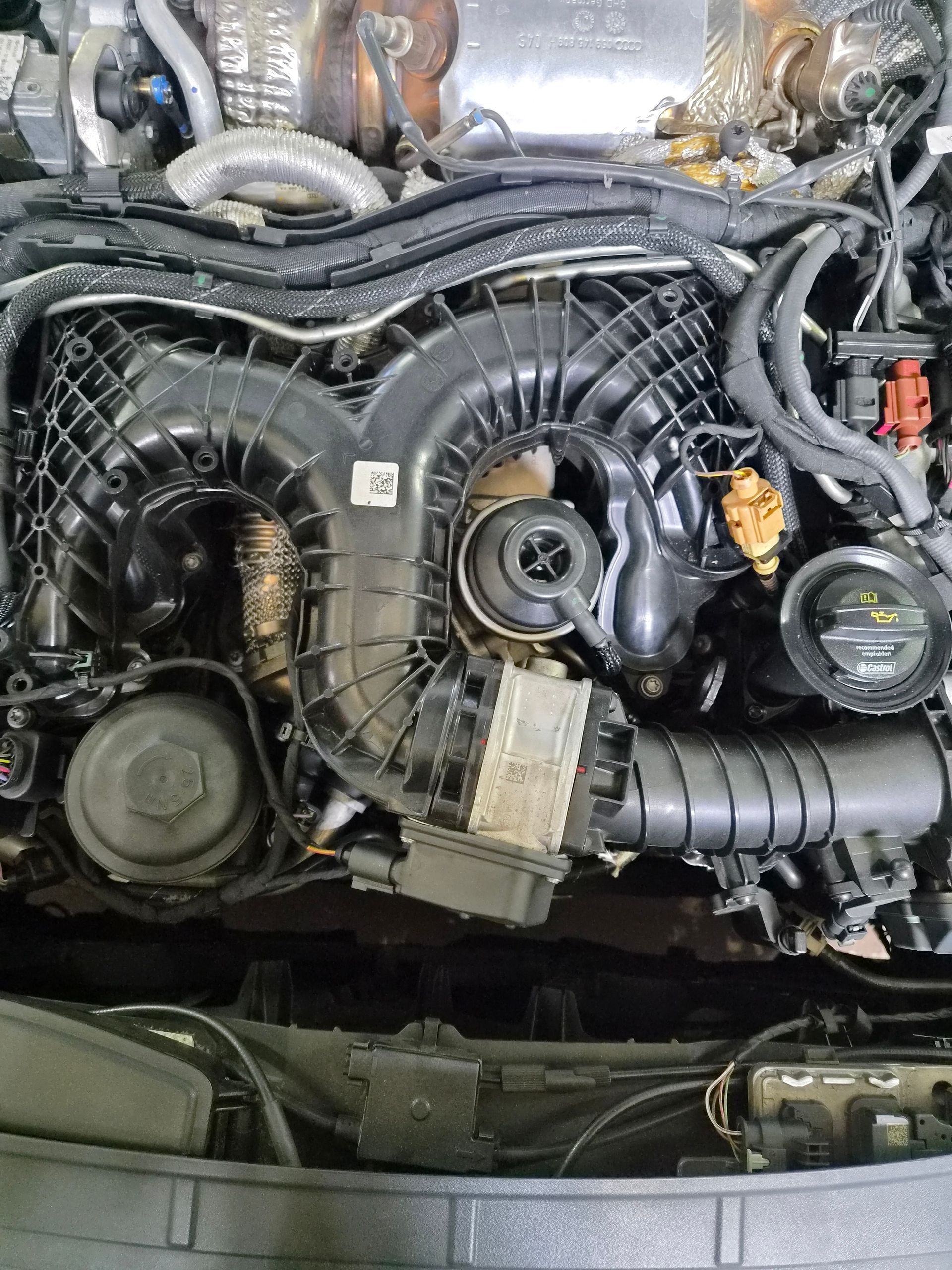 Gros plan sur le compartiment moteur d’une voiture, avec des durites d’admission en plastique noir et des composants visibles