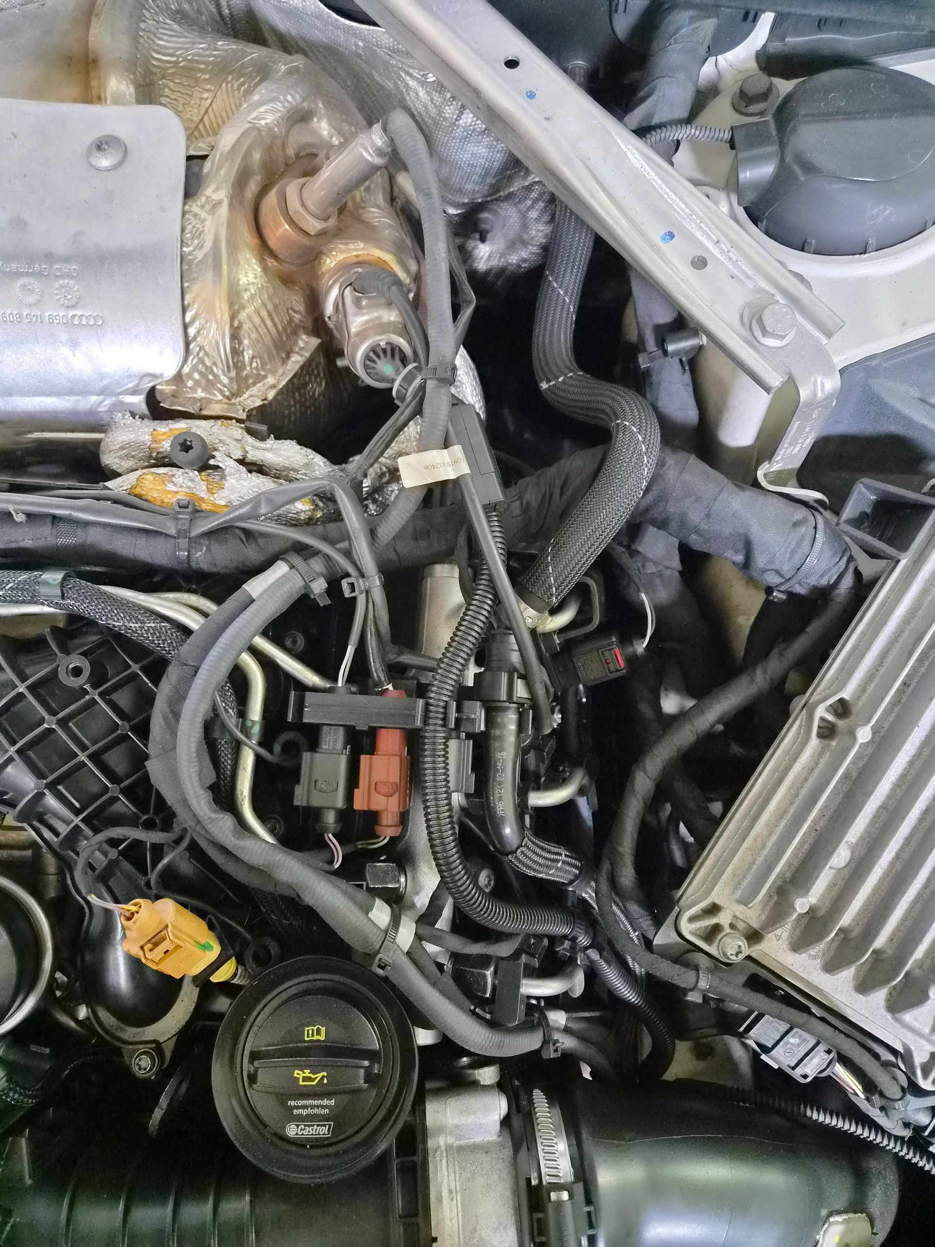 Compartiment moteur d’une voiture, avec câblage, durites et pièces métalliques apparents, vu de dessus.