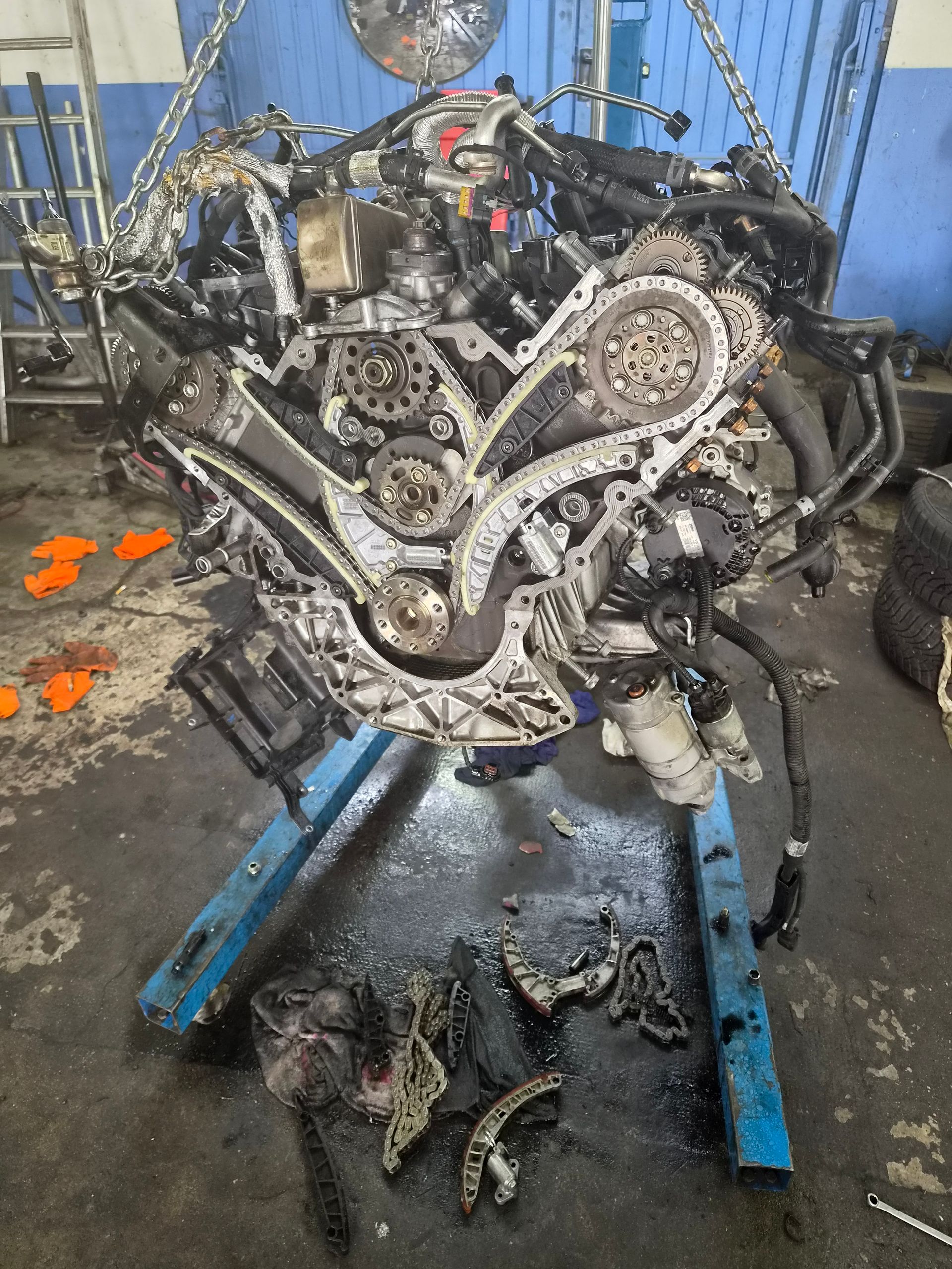 Moteur de voiture démonté sur un support bleu dans un atelier, avec des pièces éparpillées sur le sol.