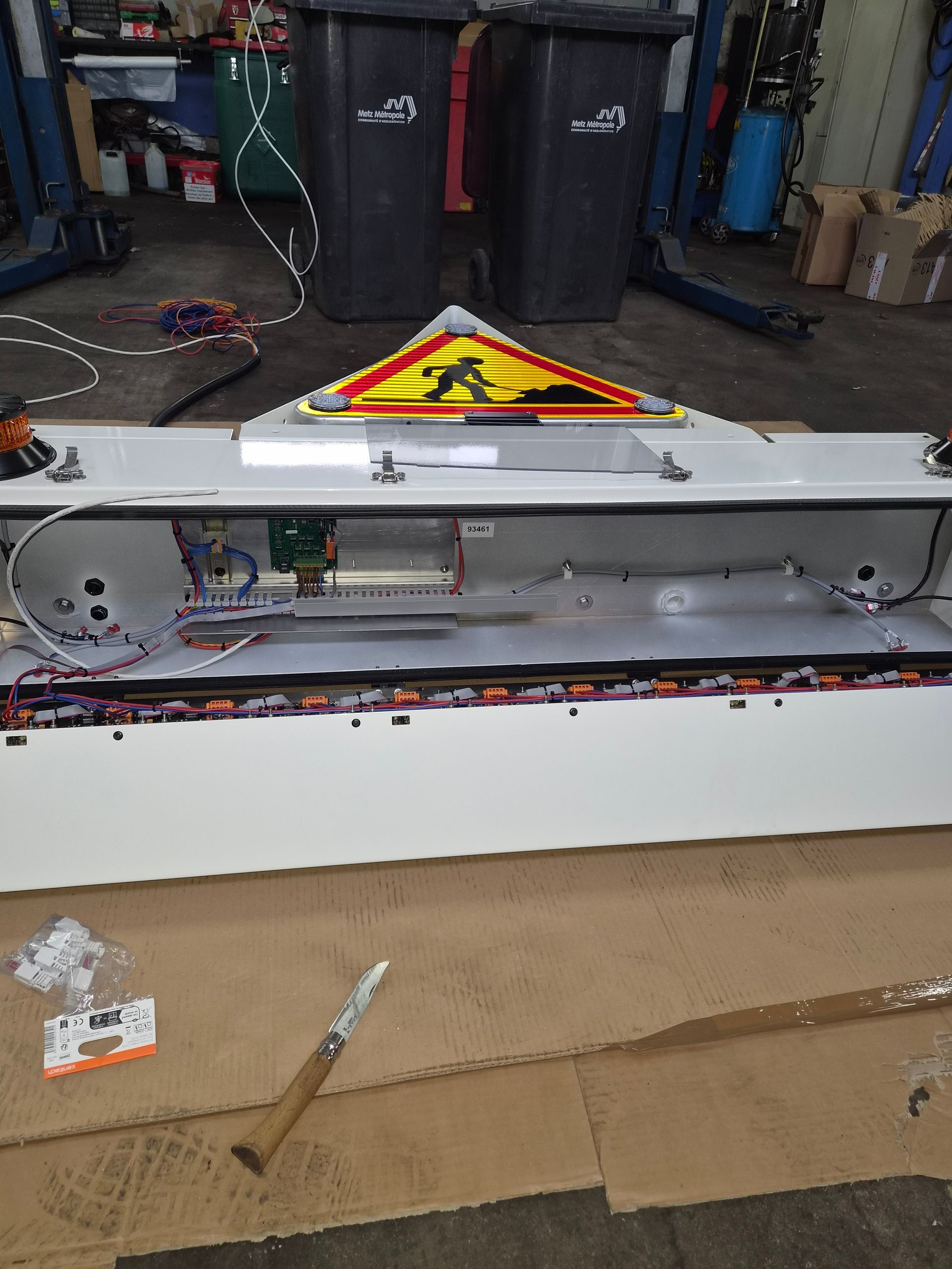 Appareil électronique ouvert sur un établi, avec un panneau d’avertissement, dans un atelier ressemblant à un garage