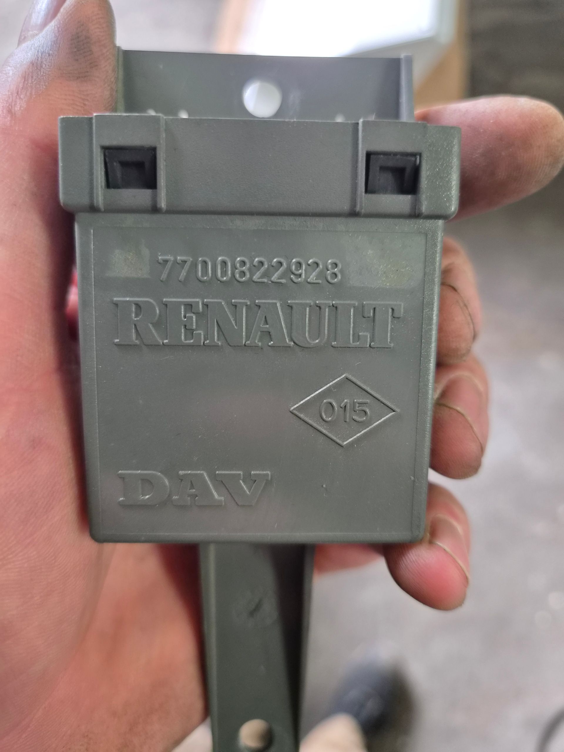 Gros plan d’une pièce automobile en plastique grise Renault D15 tenue dans une main.