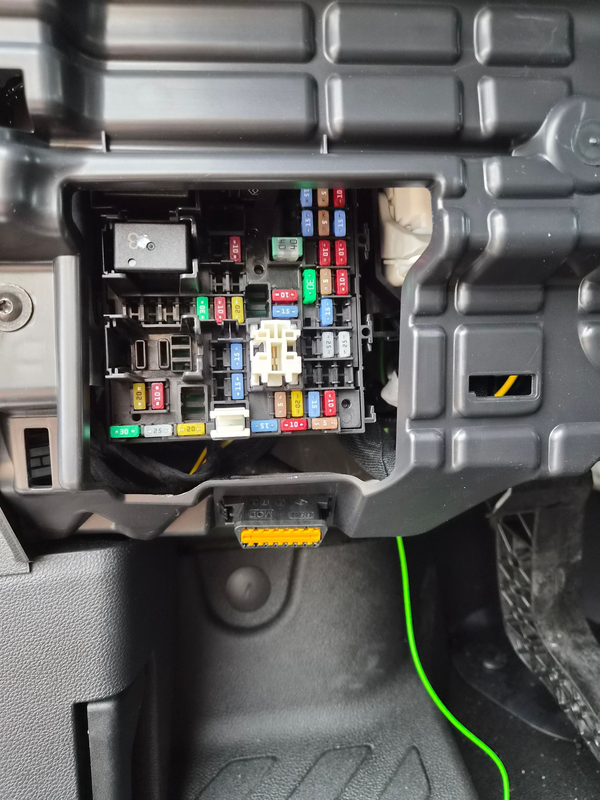 Boîtier à fusibles du tableau de bord d’une voiture, avec des fusibles et des relais colorés visibles derrière un panneau