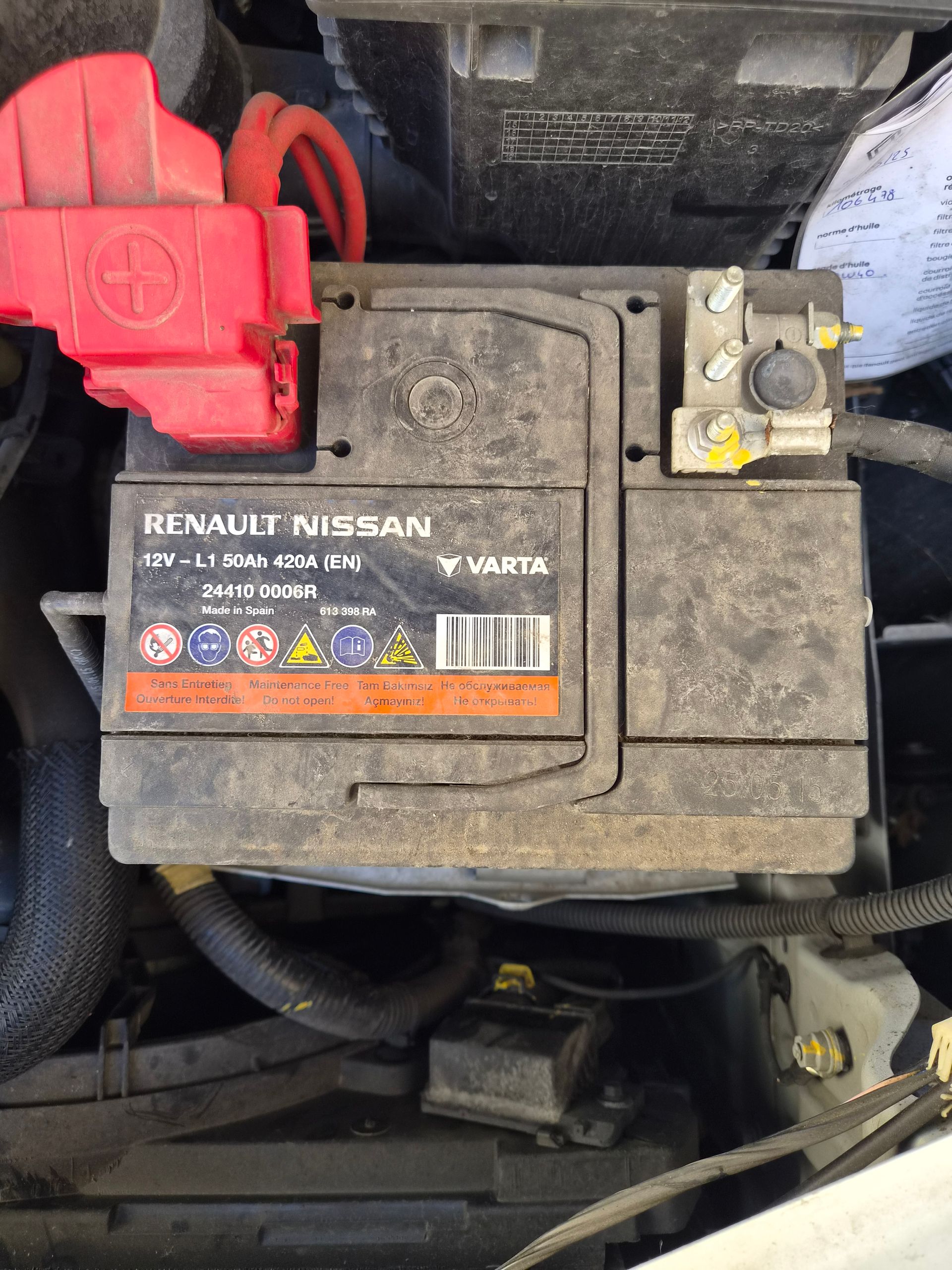 Batterie de voiture sale avec cache rouge sur la borne et étiquette Renault Nissan sous le capot