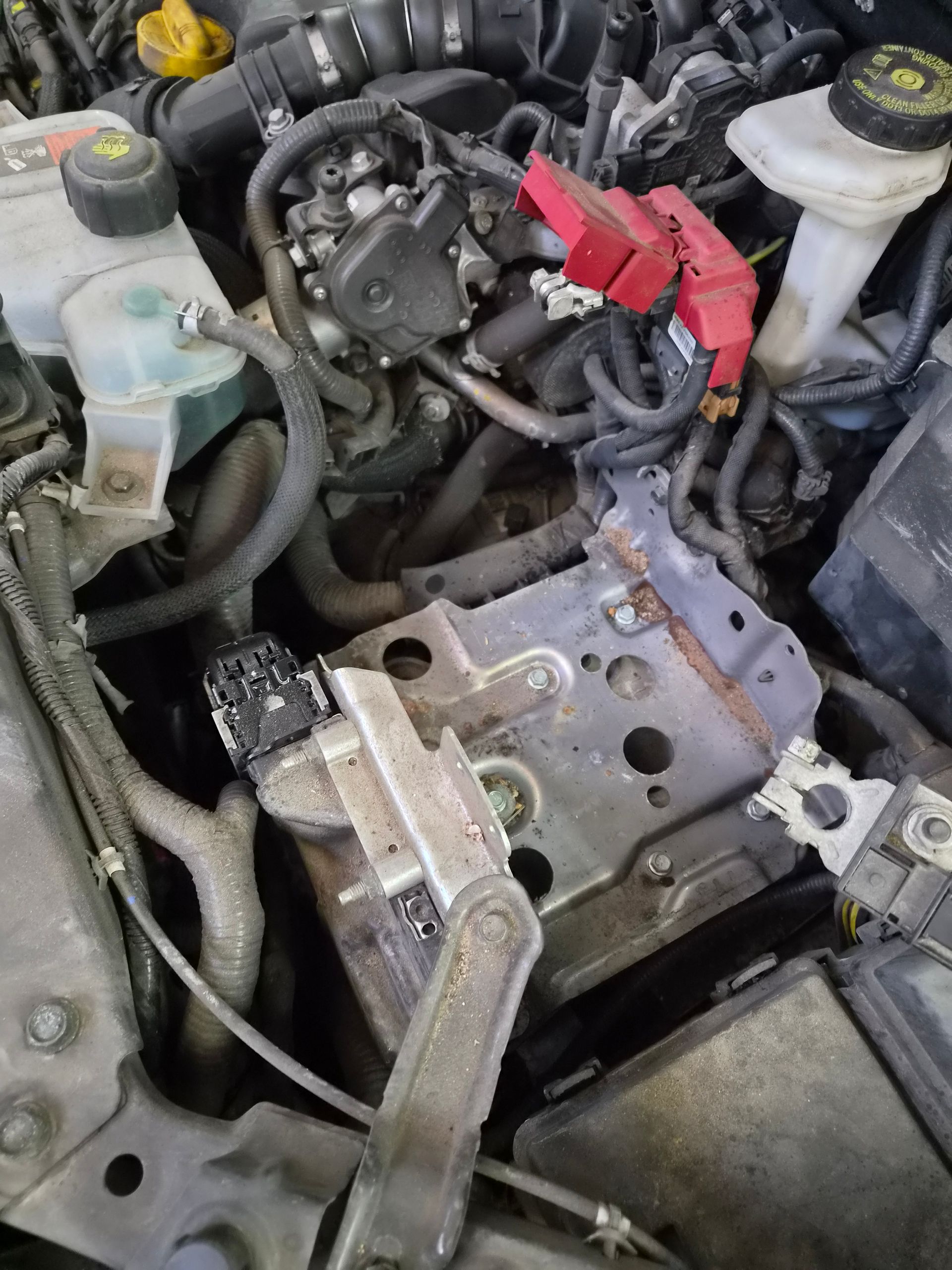 Compartiment moteur ouvert, avec le support de batterie retiré et des câbles de démarrage rouges près des pièces du moteur