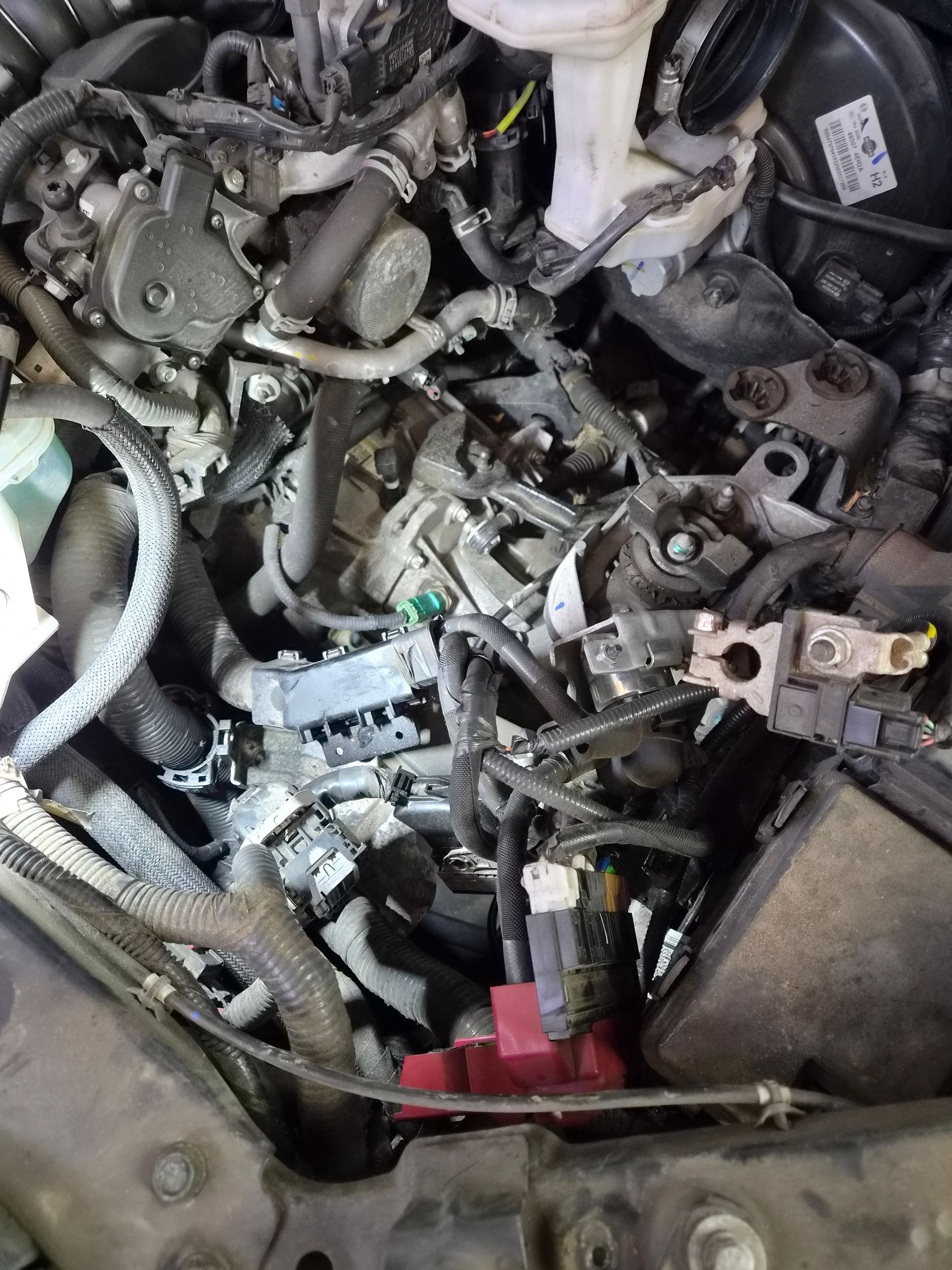 Gros plan sur le compartiment moteur d’une voiture, avec des câbles, des durites et des pièces métalliques apparents.