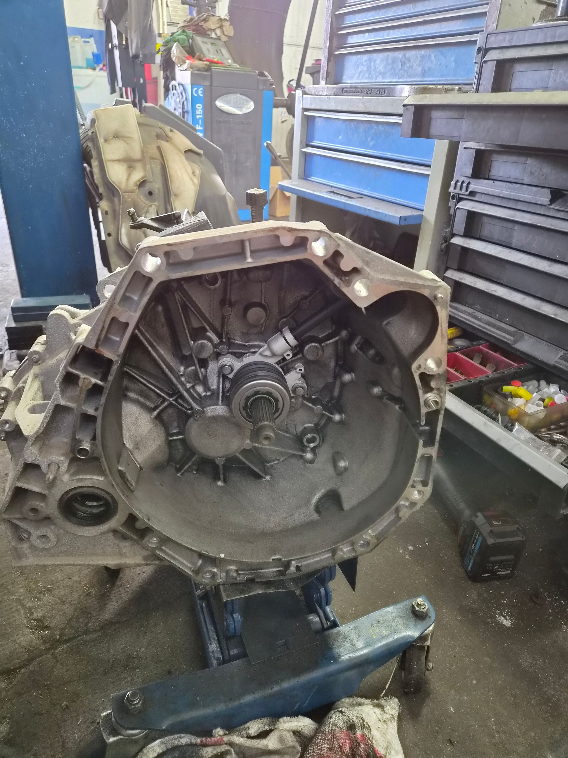 Boîte de vitesses de voiture montée sur un support dans un atelier, avec des outils et des armoires de rangement bleues à proximité