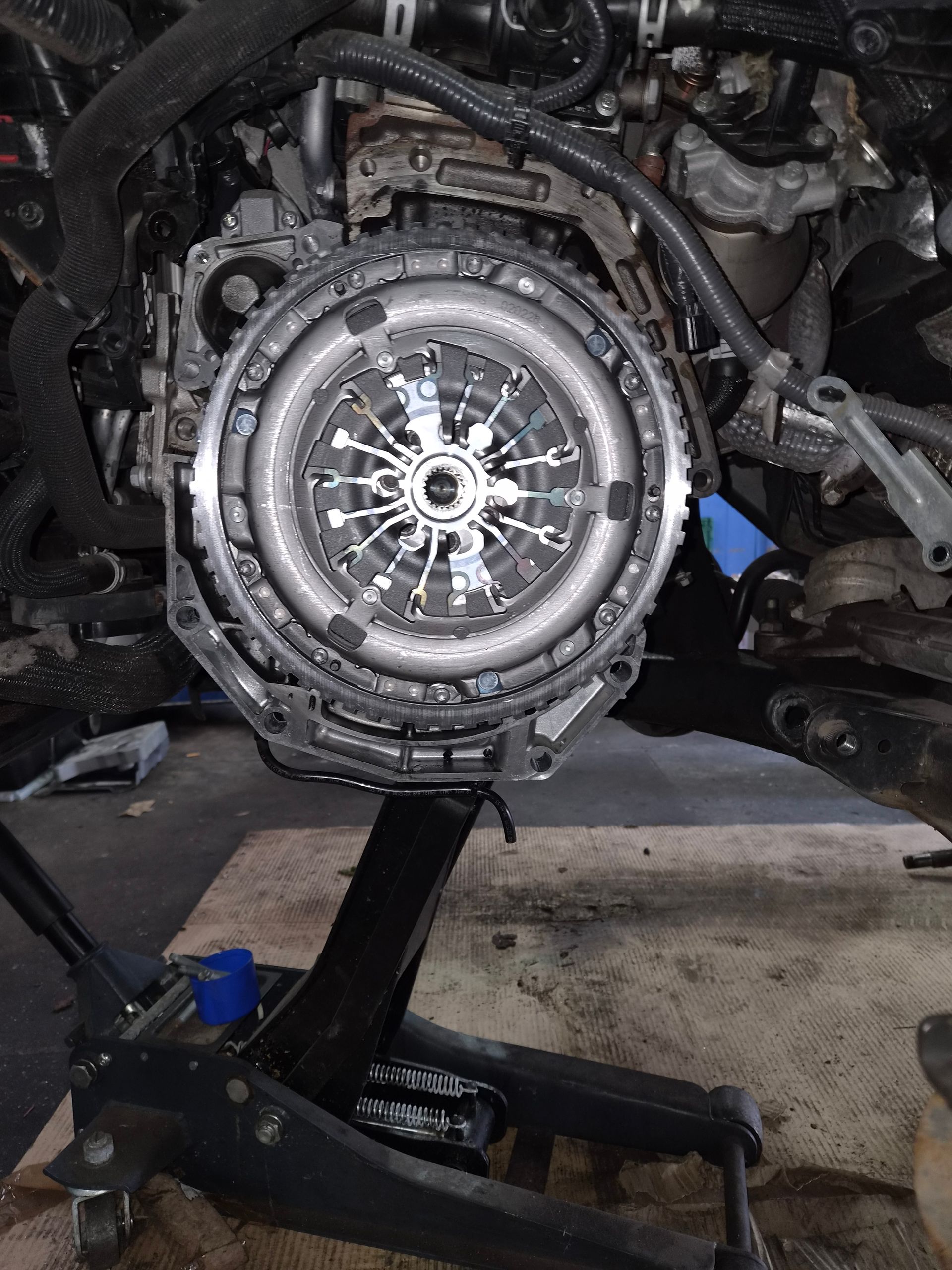 Moteur de voiture déposé et soutenu par un cric dans un garage, avec l’embrayage et le volant moteur visibles.