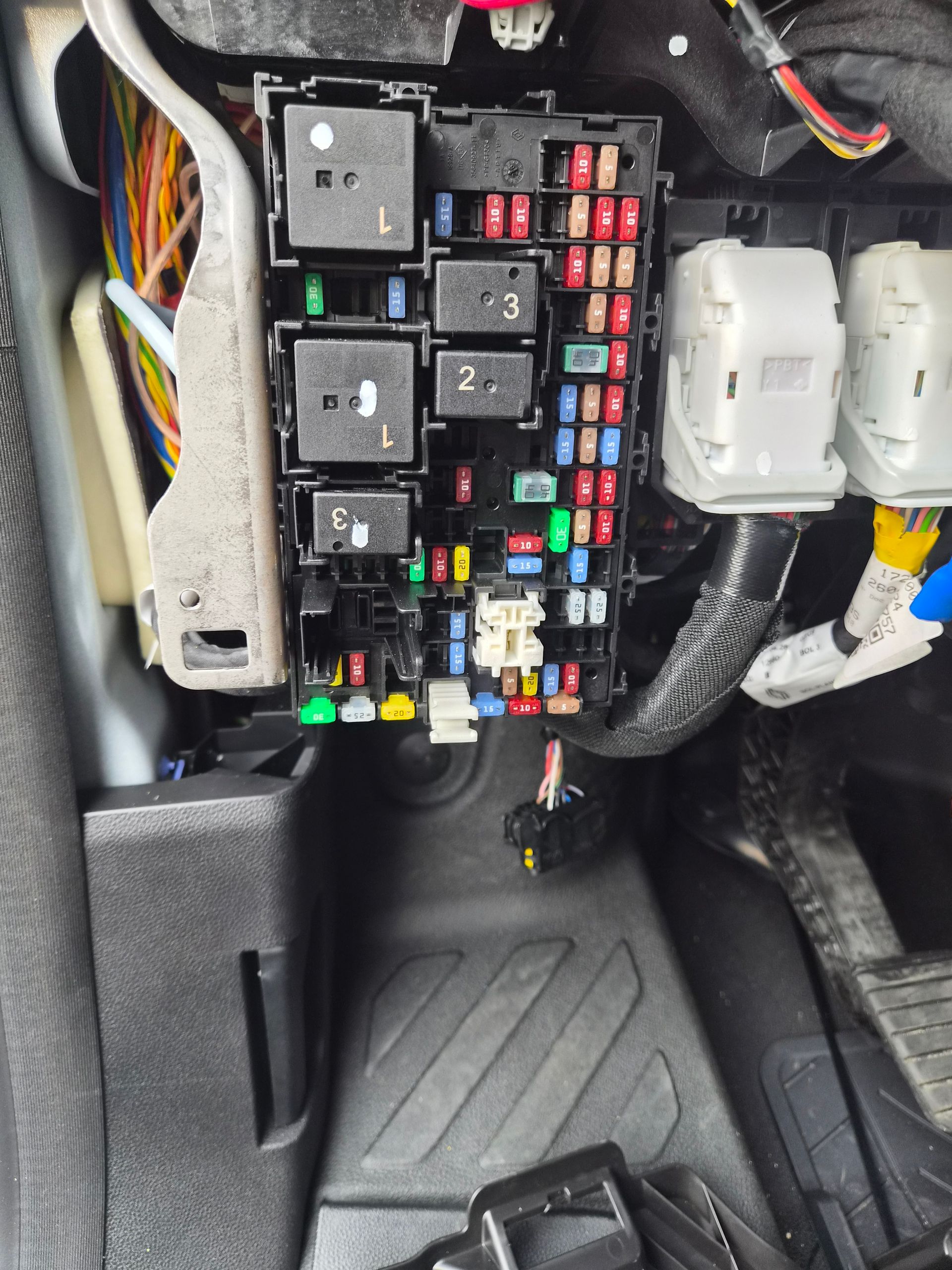 Boîte à fusibles de voiture avec des fusibles et des relais colorés sous le tableau de bord, près du repose-pieds.