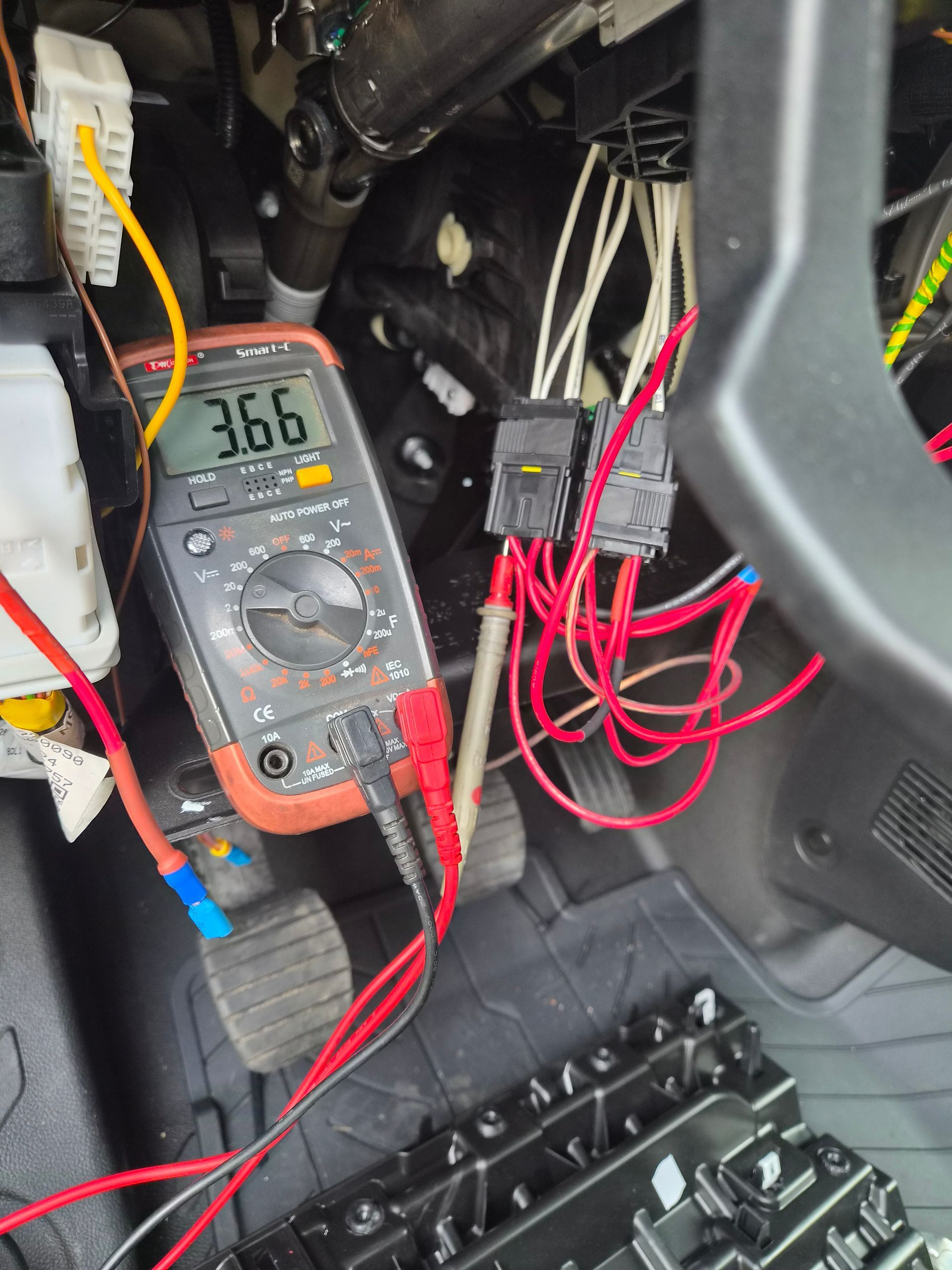 Test de fils avec un multimètre sous le tableau de bord d’une voiture, avec des pointes rouges et des fils dénudés