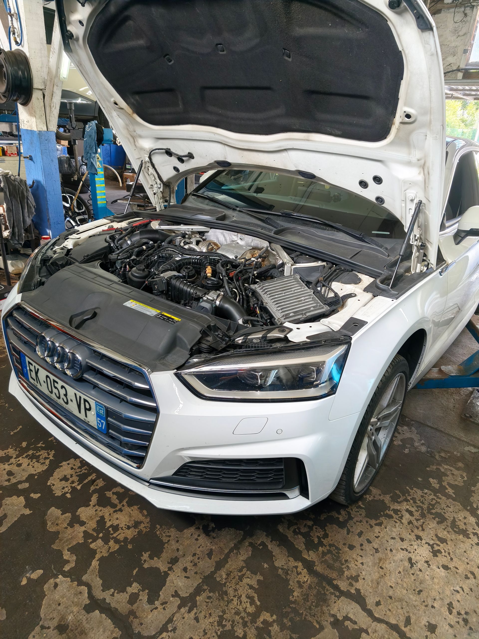 Berline blanche, capot ouvert dans un garage automobile, moteur à découvert pendant une réparation.