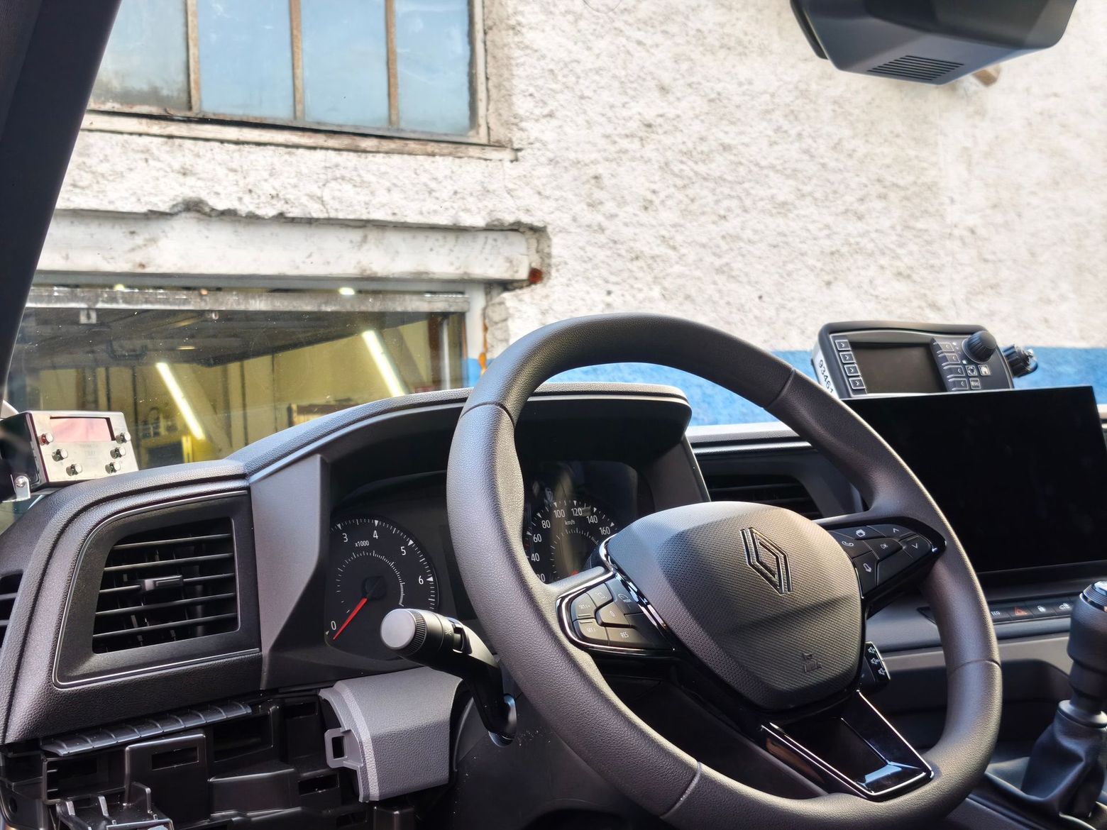 Intérieur de voiture avec volant et tableau de bord, garée à côté d’un bâtiment dont la porte de garage est ouverte