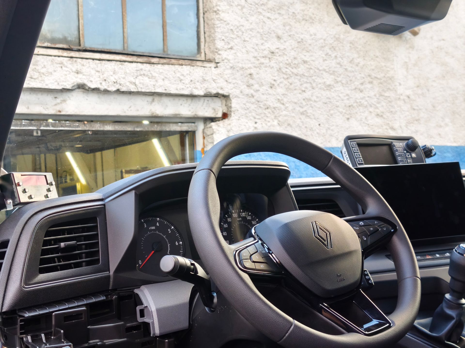 Intérieur de voiture avec volant et tableau de bord, garée près d’un bâtiment et d’une porte de garage ouverte