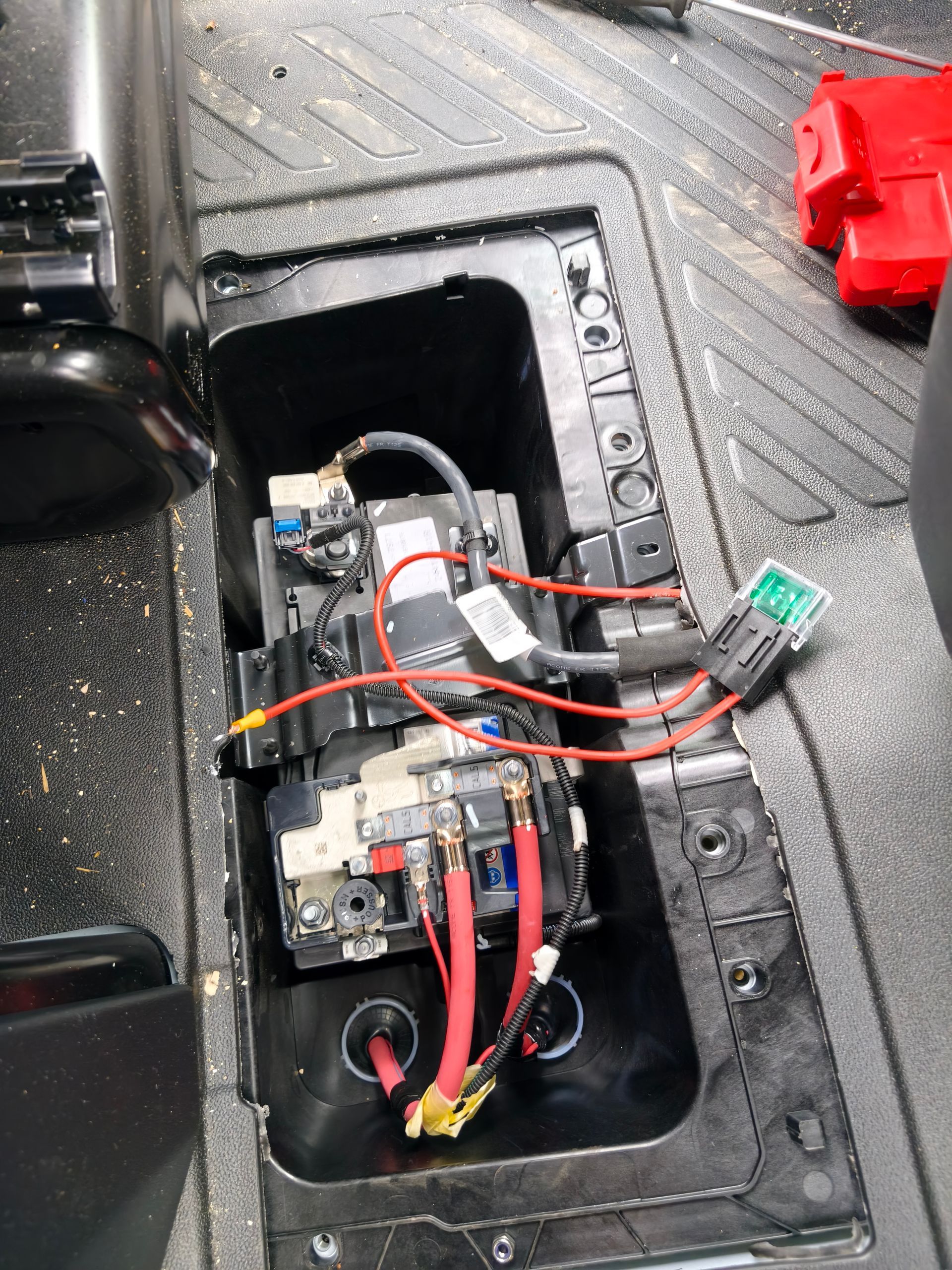 Compartiment électrique ouvert, avec des câbles et des composants à l’intérieur d’un boîtier en plastique noir posé sur un sol texturé.