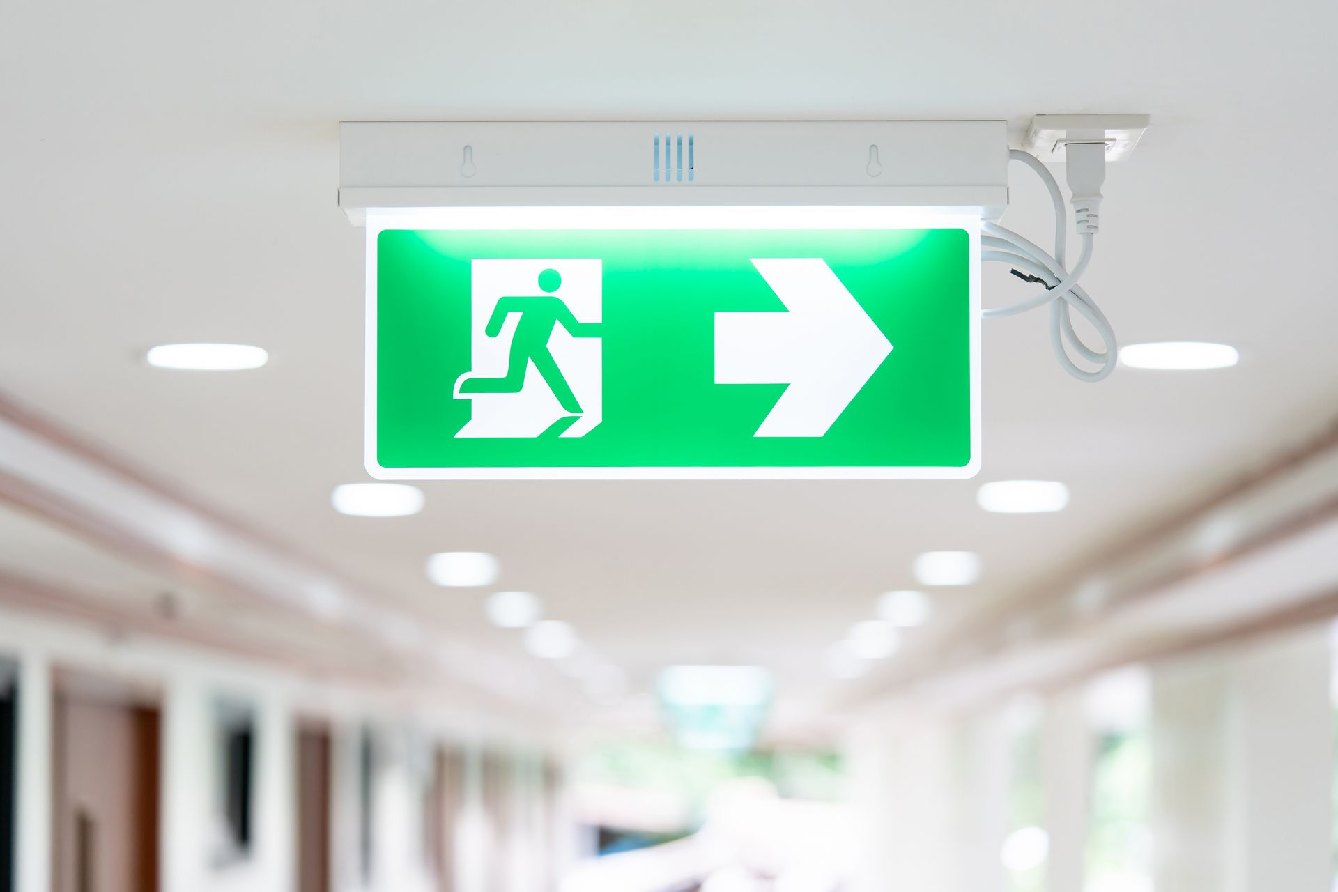 Panneau de sortie de secours vert lumineux avec une silhouette courant et une flèche pointant vers la droite au plafond d'un couloir